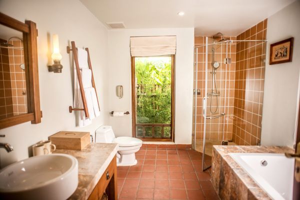 Bathroom with white sink, toilet, and bathtub. Shower with glass door, brown tile, and open window.