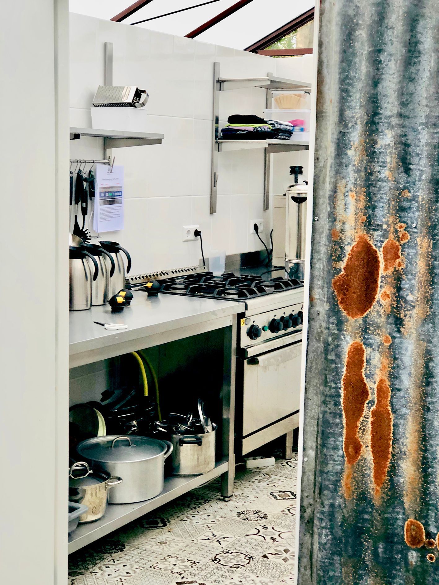 Commercial kitchen interior with stainless steel appliances, visible through a corrugated metal door.