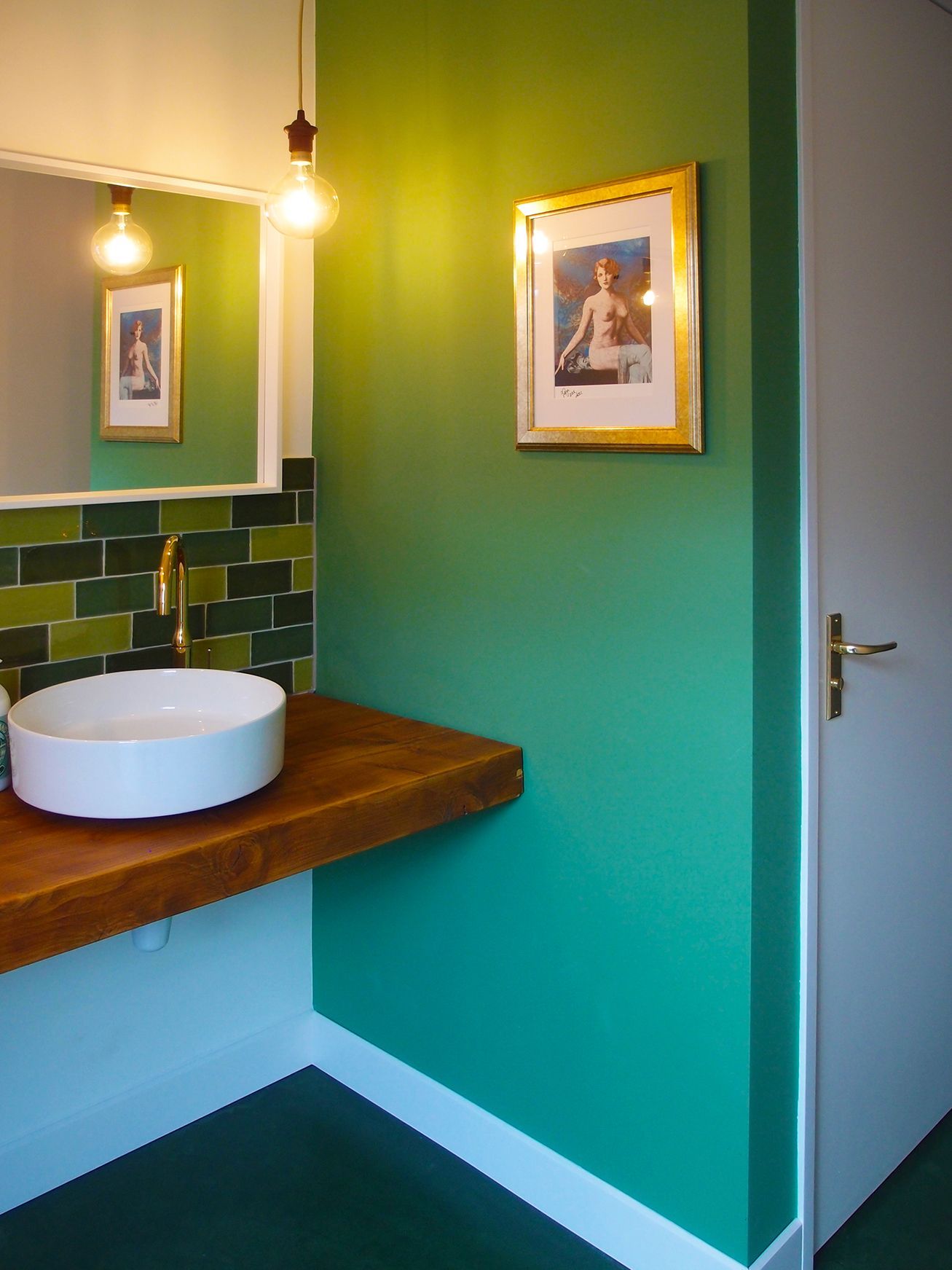Bathroom with green walls, white sink, wooden counter, gold faucet, framed art, and white door.