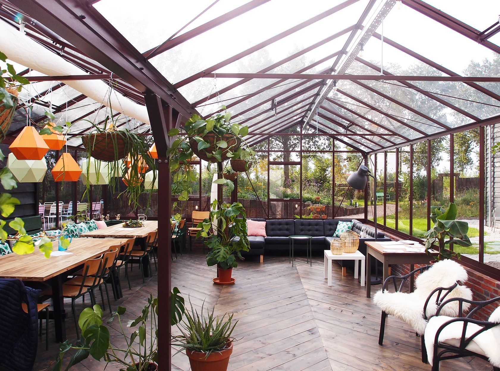 Greenhouse interior with tables, plants, and seating. Sunlight streams through glass roof.