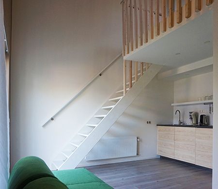 Interior with white stairs leading to a loft. Green couch and small kitchen visible.