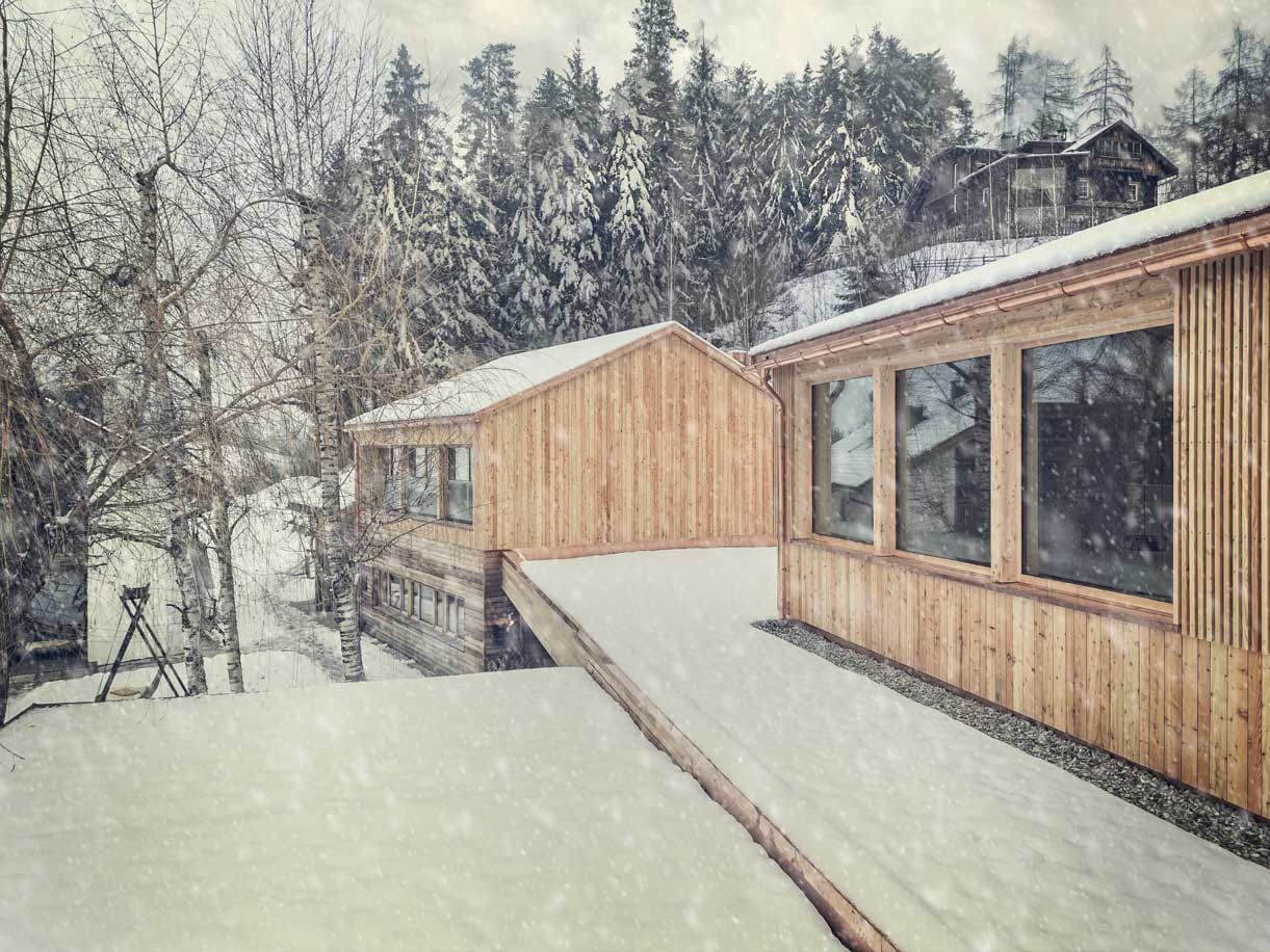 Snowy wooden buildings connected by a ramp in a winter landscape with snow-covered trees.
