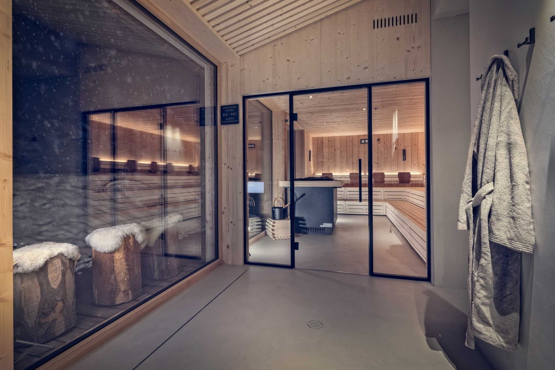 Spa interior with sauna, relaxation area, and bathrobe. Wooden accents, glass doors, and seating.