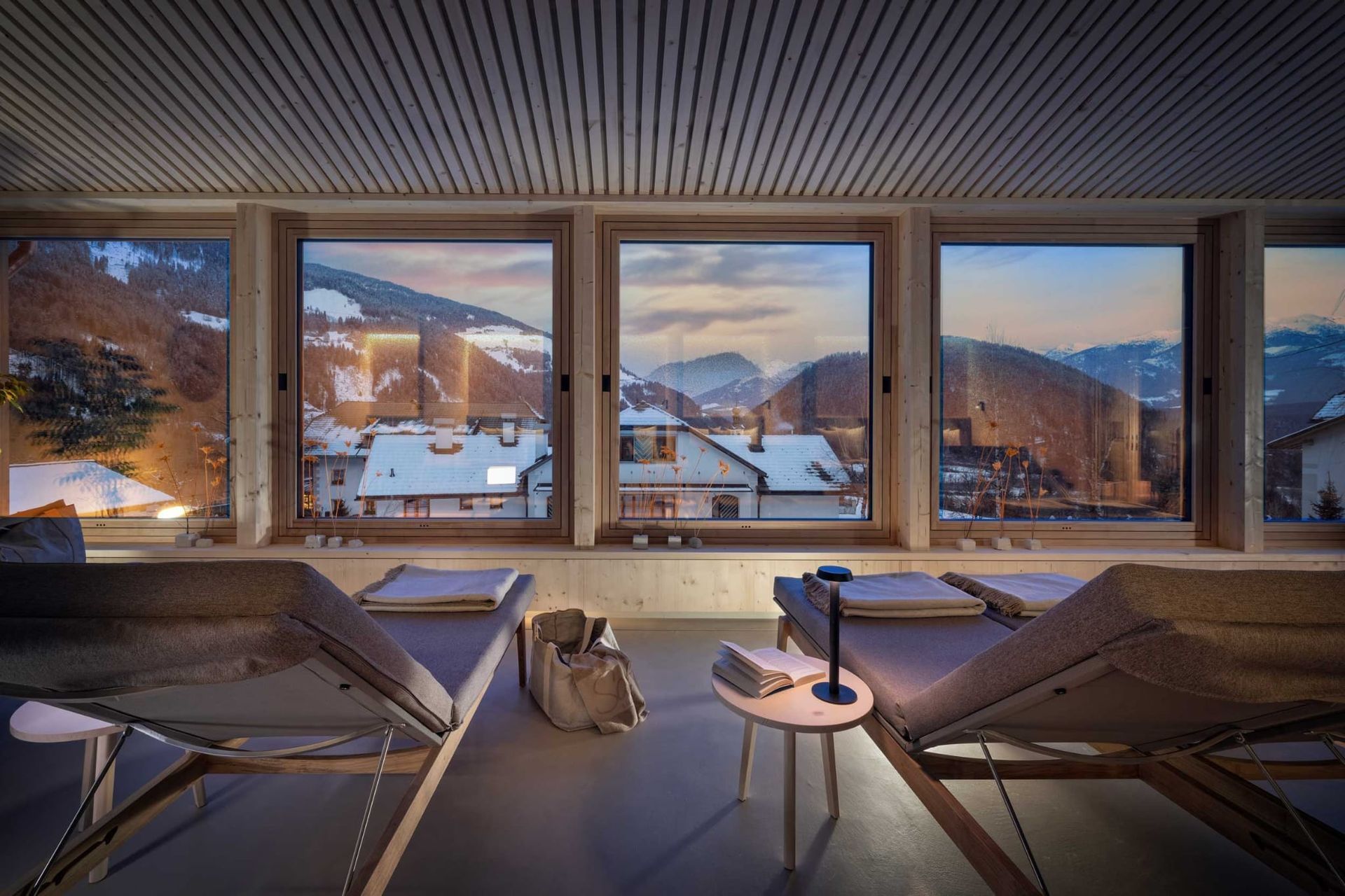 Spa lounge with window view of snow-covered mountains, two chaise lounges, and small table with lamp.