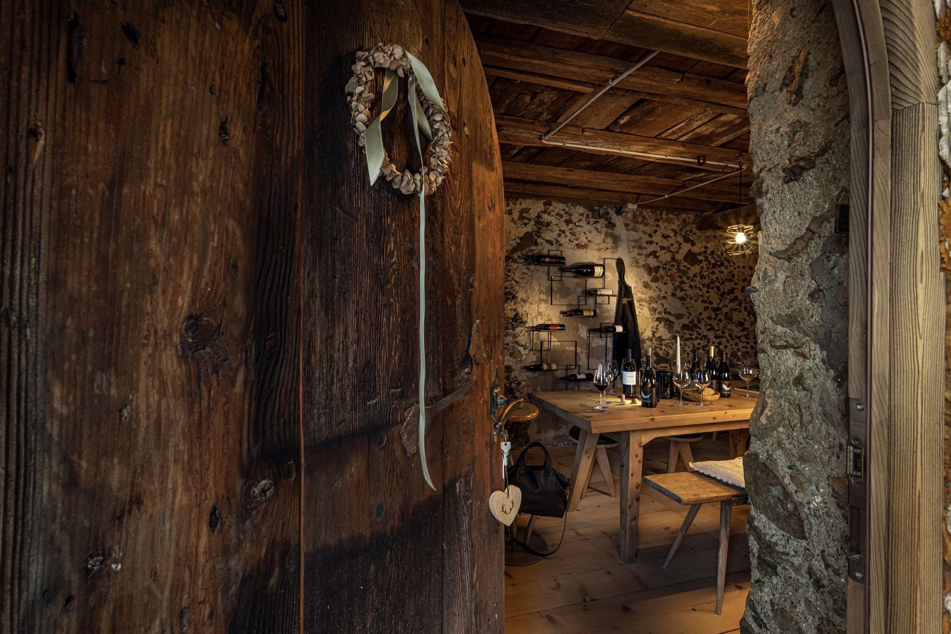 Old wooden door opens to a rustic wine cellar with a table and bottles.