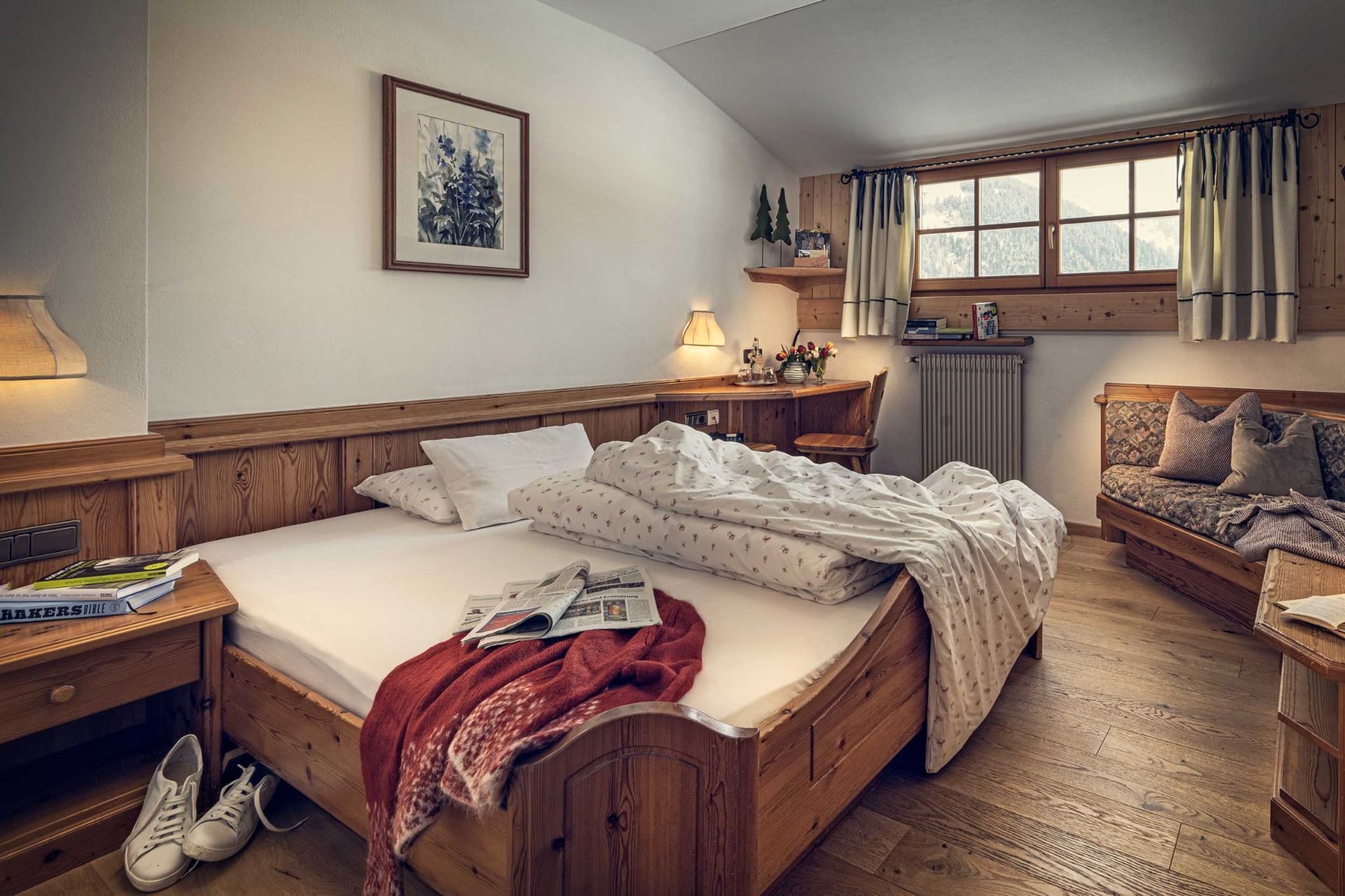 Cozy bedroom with wooden furniture, a large bed with a patterned duvet, and a small sofa near a window.