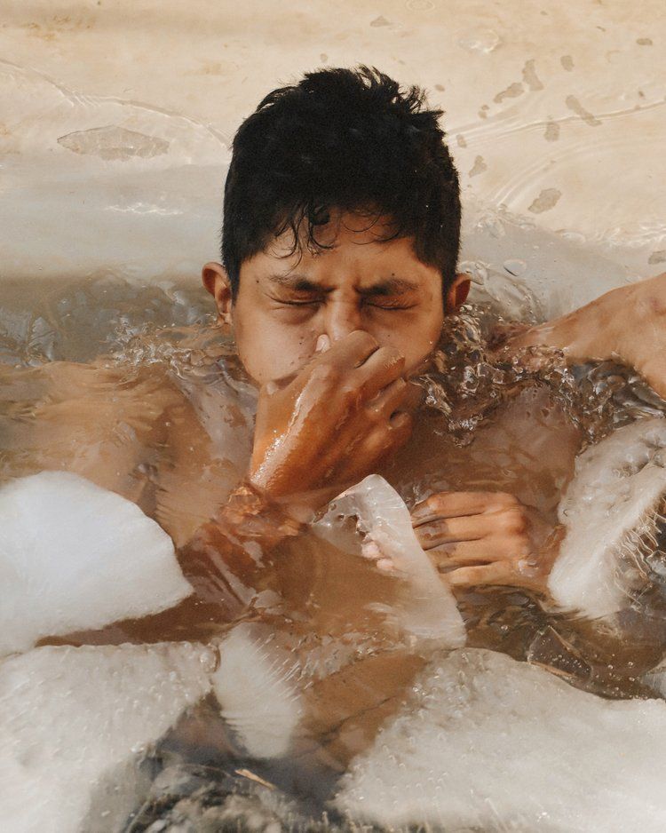 Man in cold water, eyes closed, hand covering his face. Surrounded by ice.