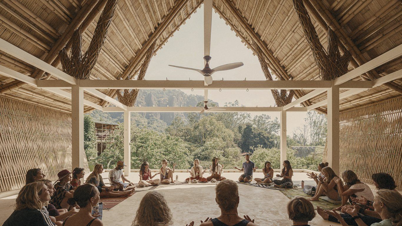 People seated in a circle, facing outward in an open-air building with thatched roof, looking at instructor.