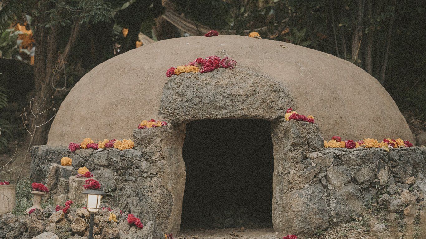 Rounded earthen structure with stone entrance decorated with orange and yellow flowers.