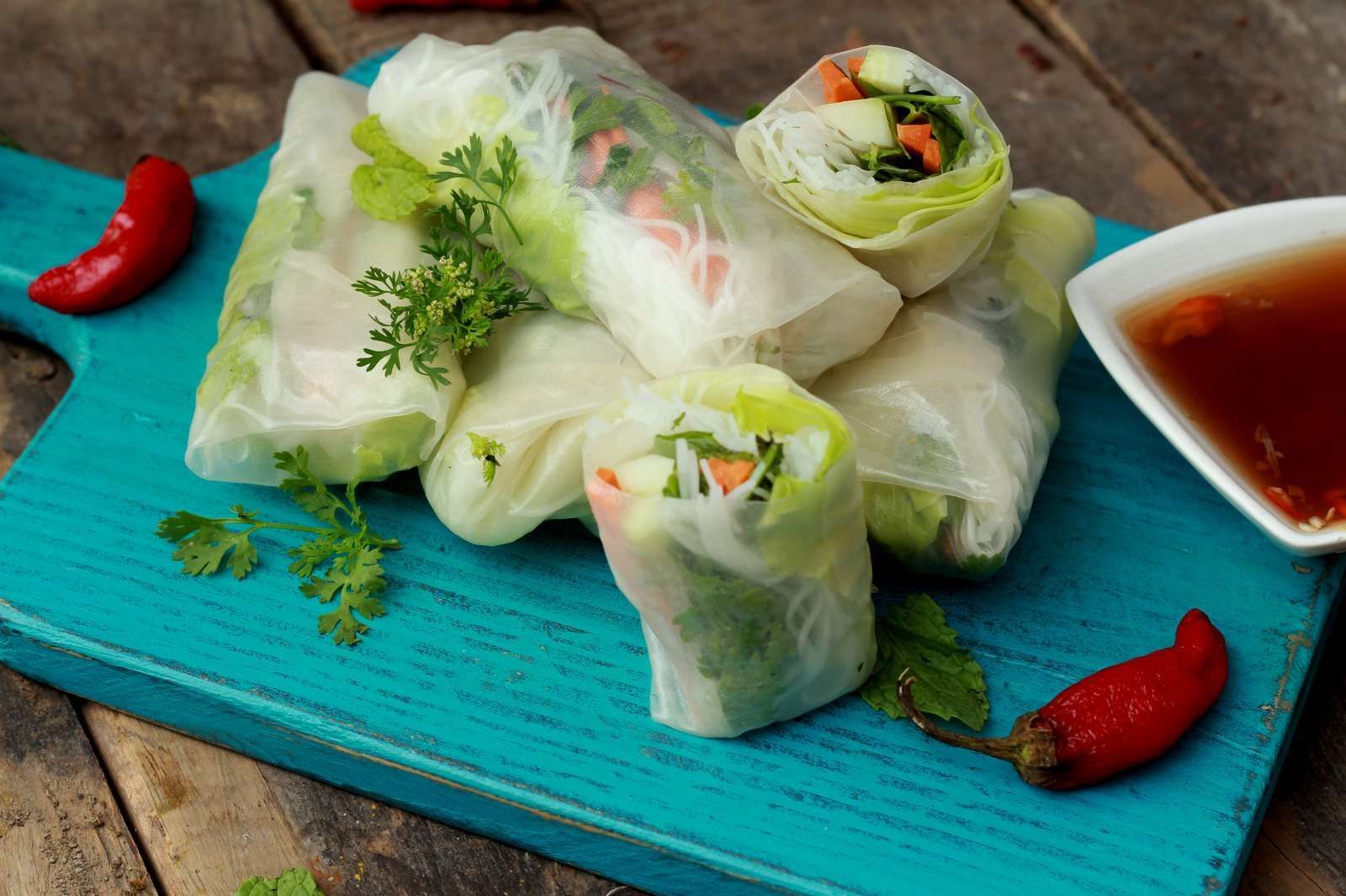 Spring rolls on a teal board with dipping sauce and red chili peppers.
