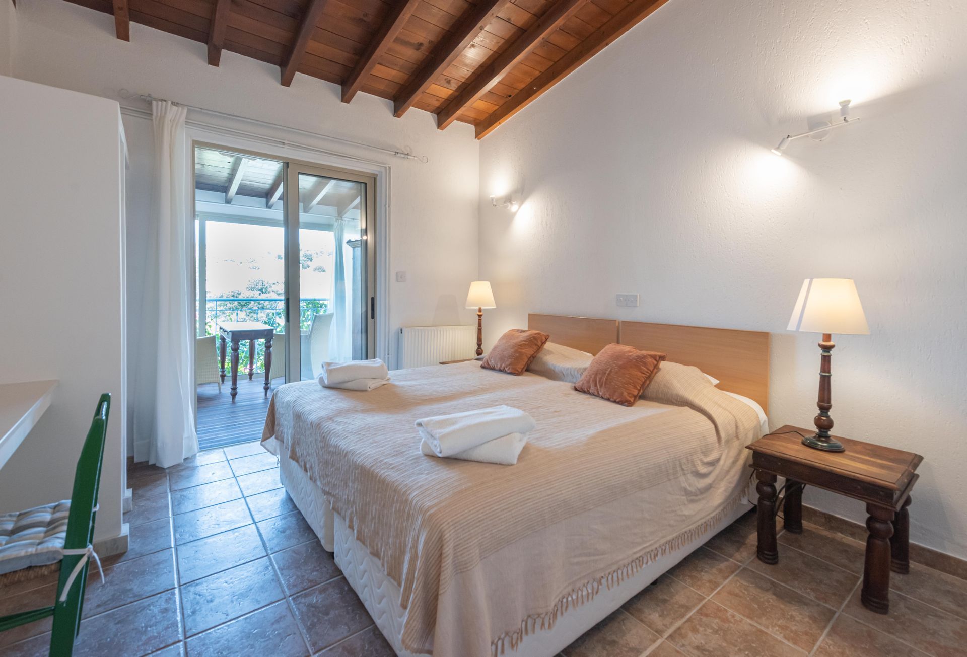 Bedroom with two beds, balcony access, wooden ceiling, and side tables.