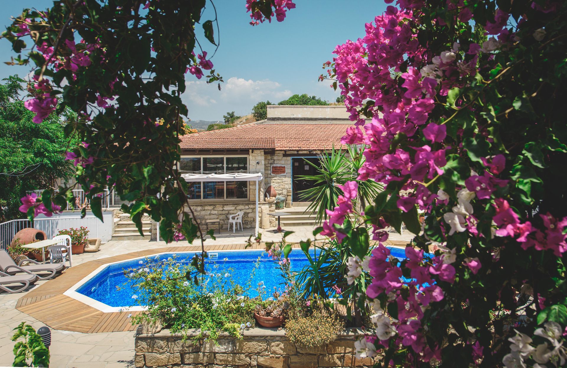 A pool with blue water in front of a stone building with pink flowers in the foreground.