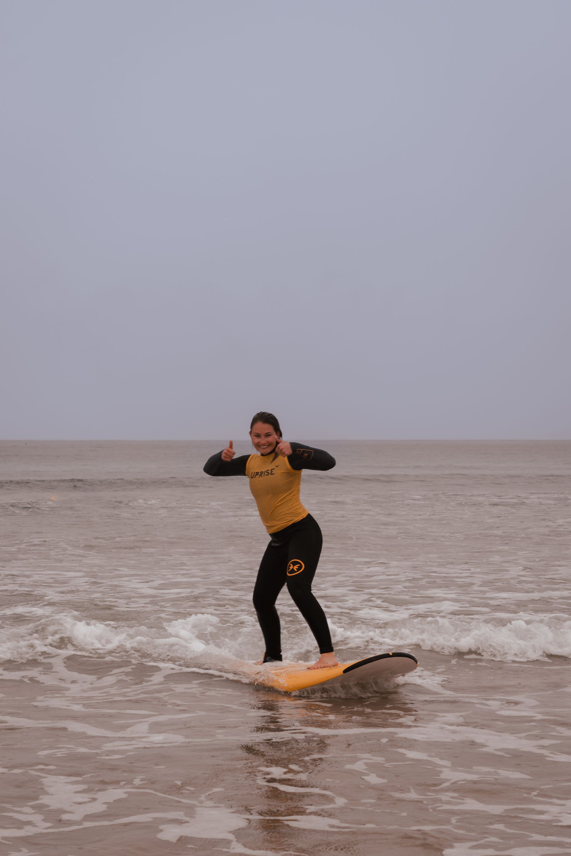 Person surfing in the ocean, wearing a yellow wetsuit, grey sky.