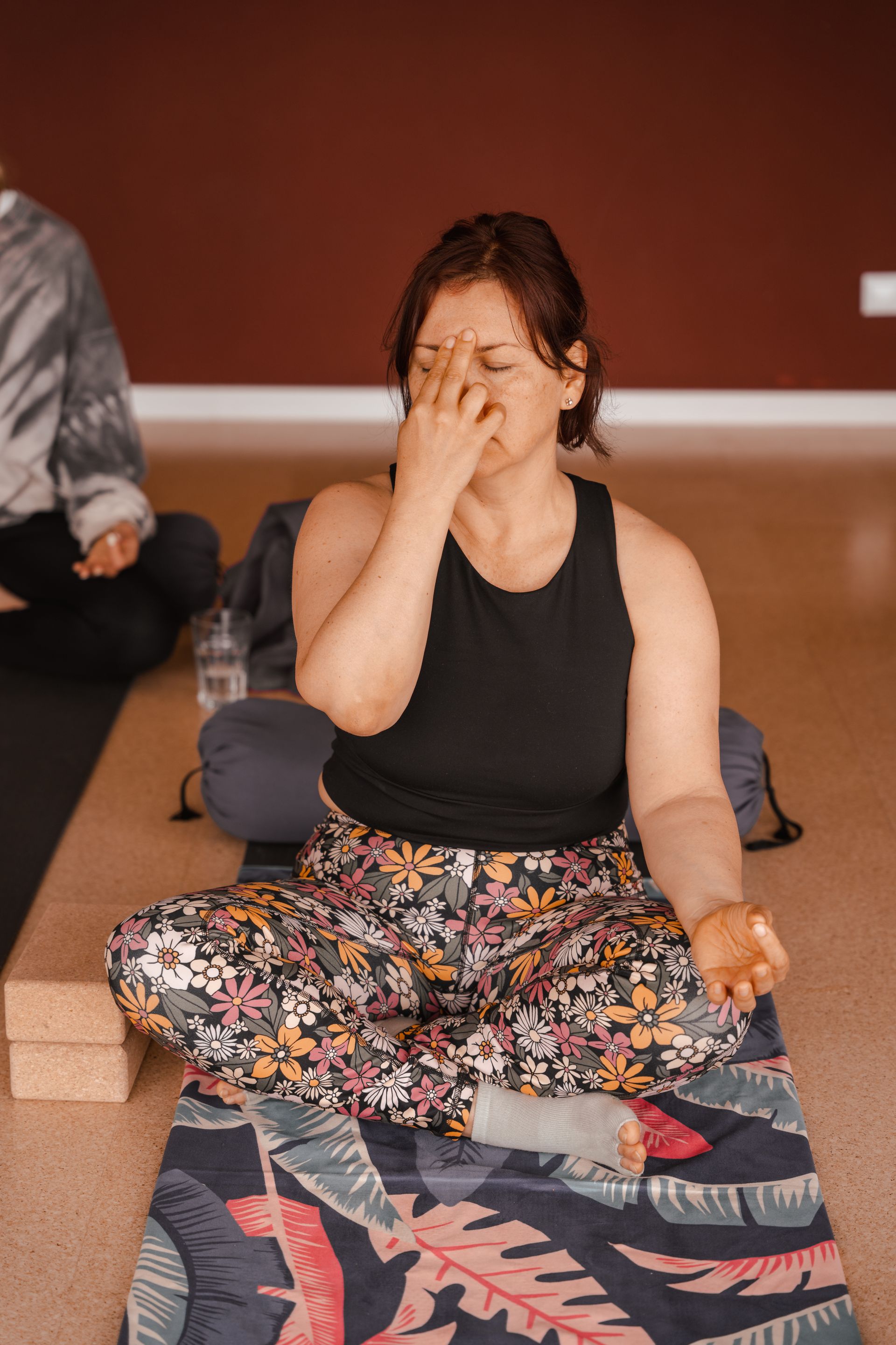 Woman in yoga pose, practicing alternate nostril breathing. Indoor setting with a maroon wall.