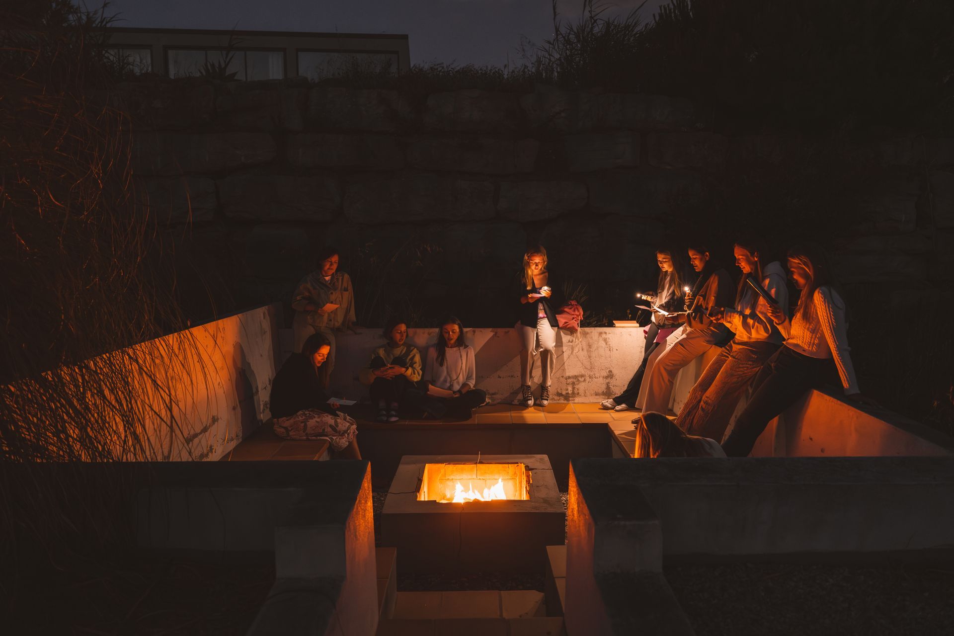 People gather around a fire pit outdoors at night.