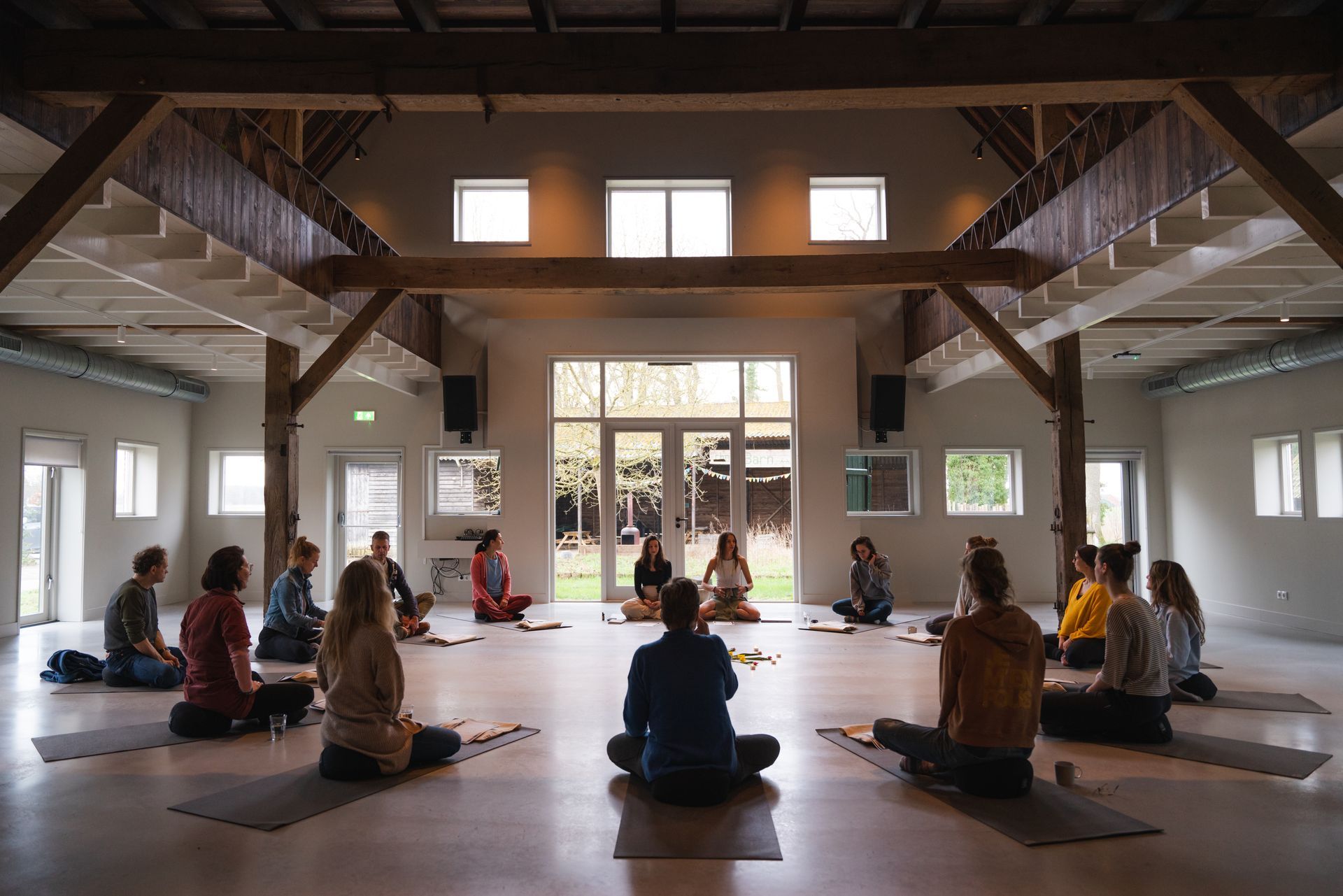 People seated in a circle meditating in a large, bright room with high ceilings.
