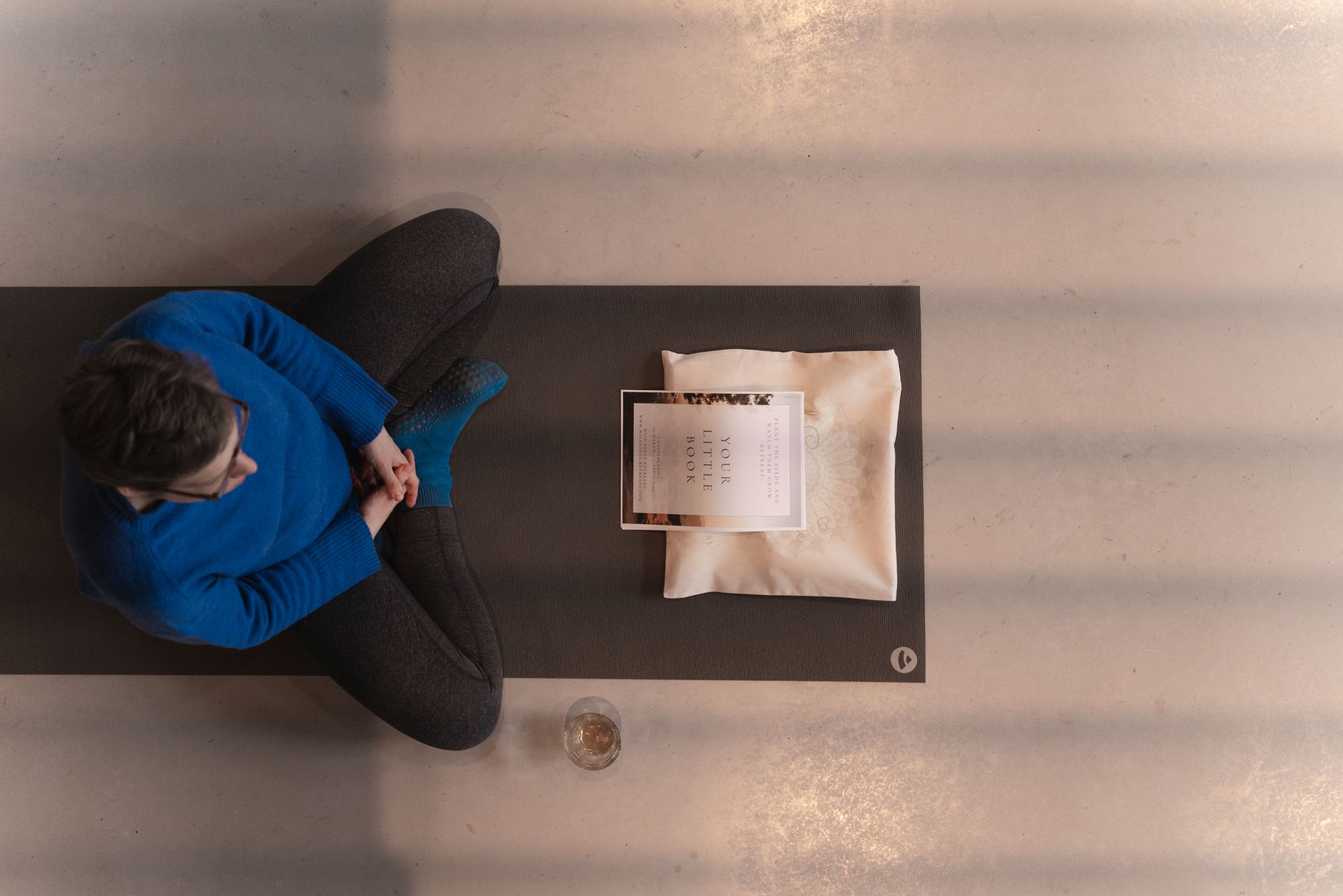 Person sits cross-legged on a yoga mat, next to a folded blanket and a card.