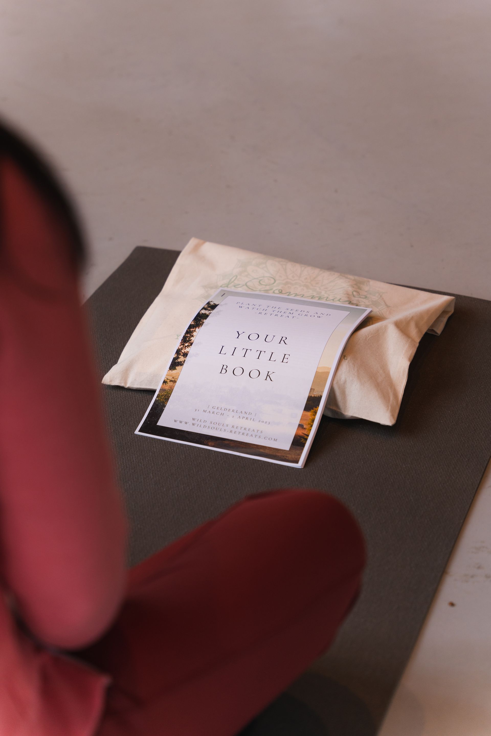 Person seated on yoga mat, looking at document on pillow; neutral interior.