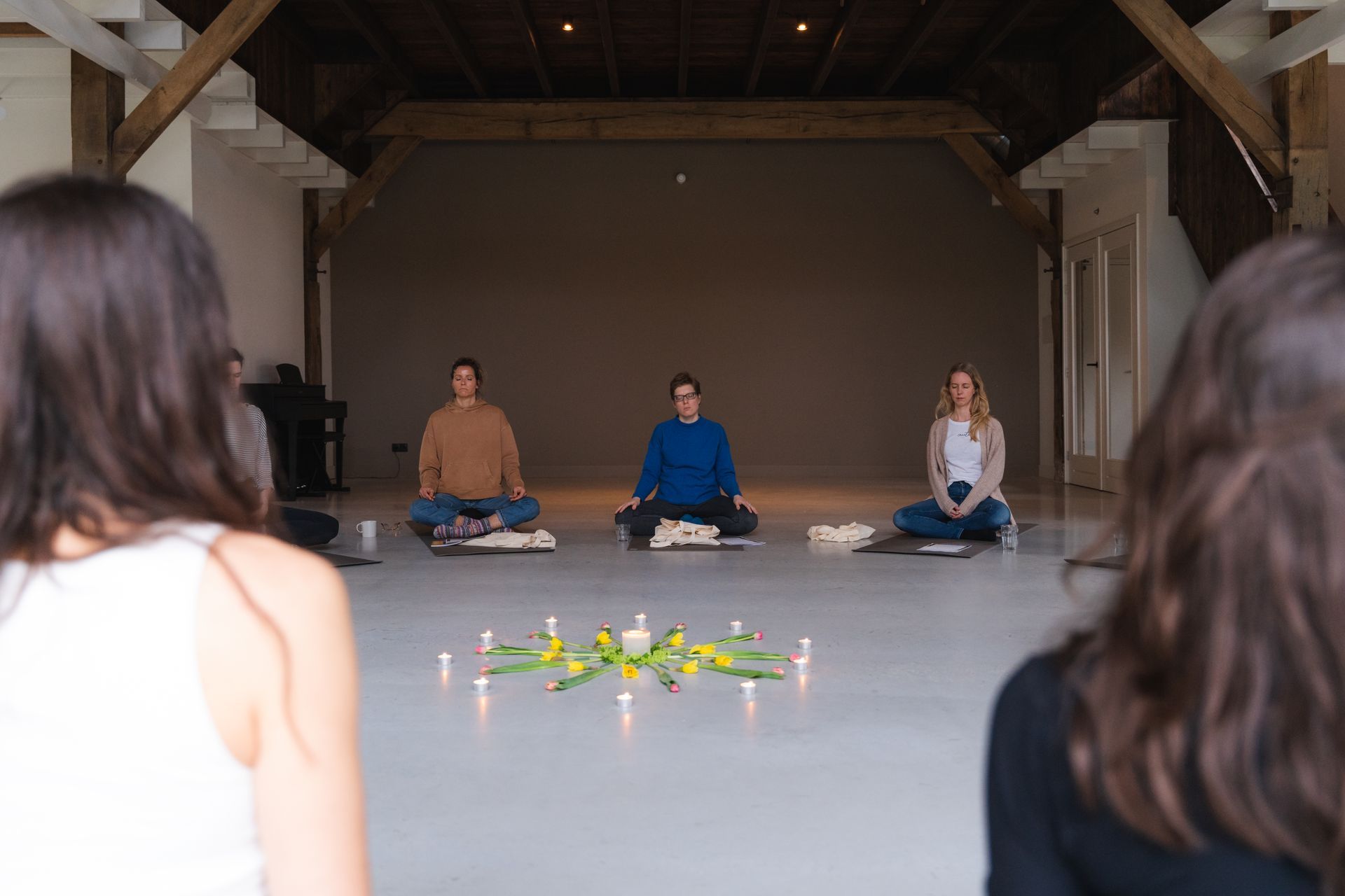 People in meditation posture, candles and flowers arranged on a floor in an open space.