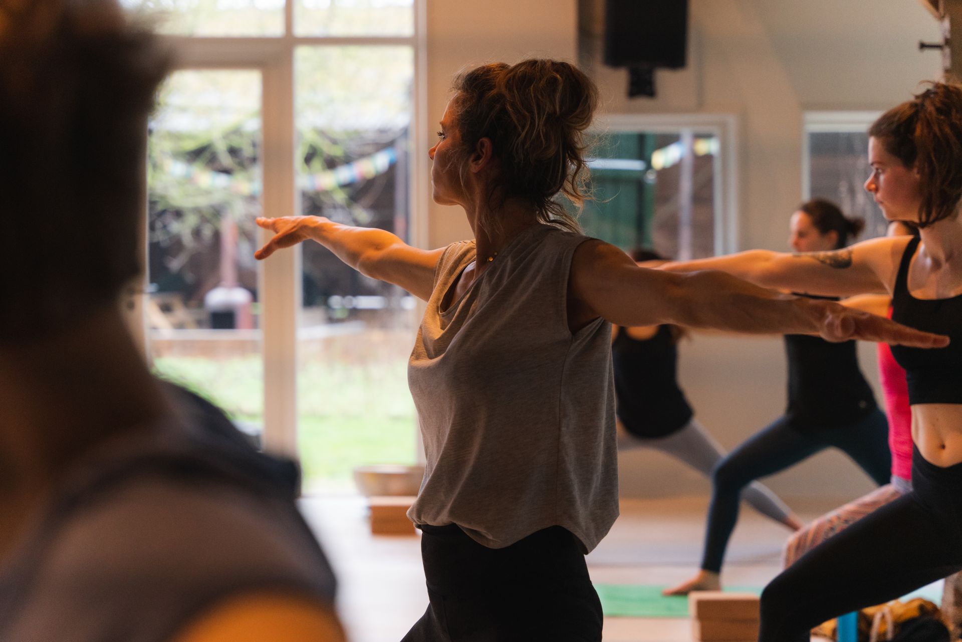 Yoga class in progress. People in workout clothes, arms outstretched, indoors.