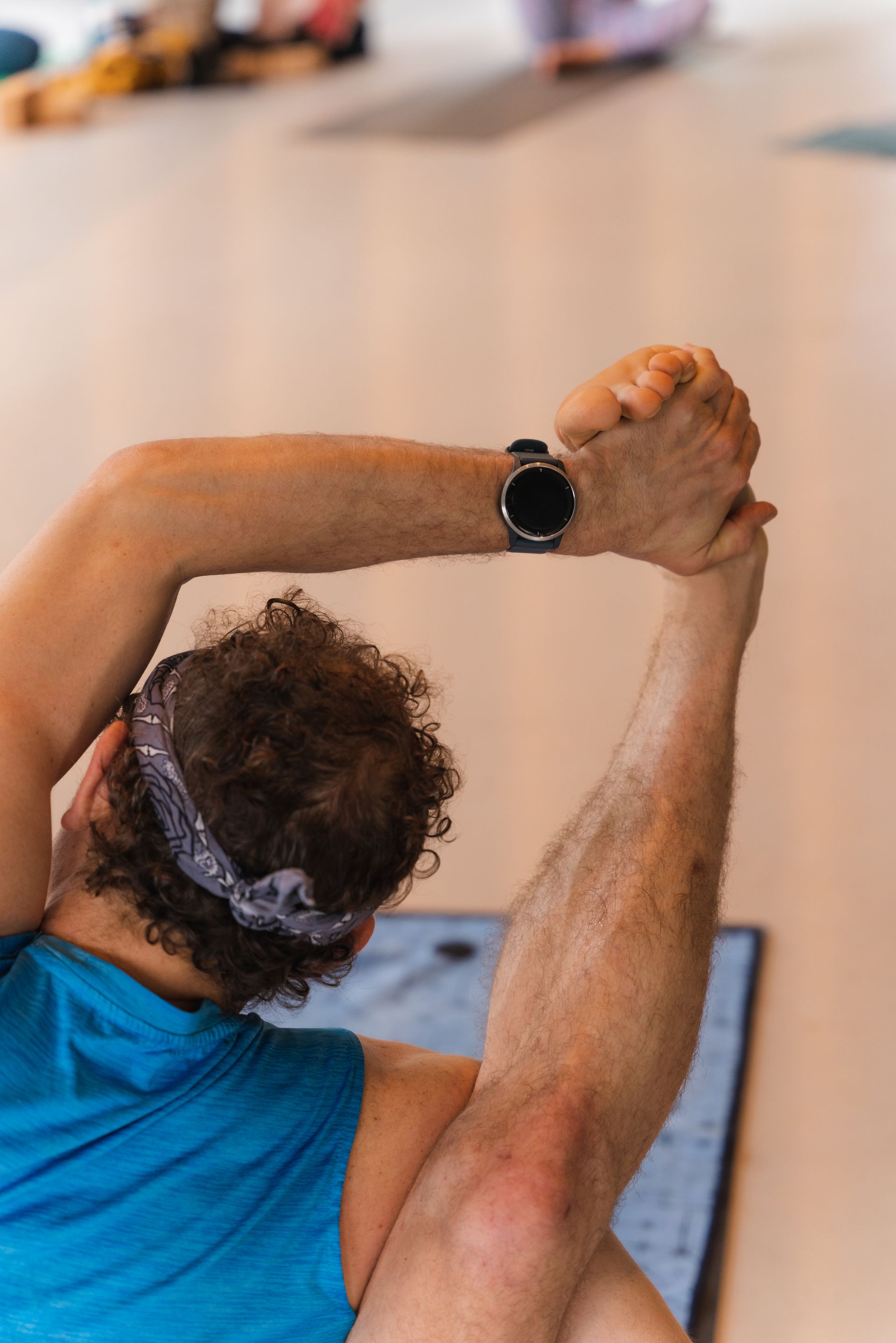 Person in yoga pose, arm raised, holding foot. Wearing headband and smartwatch.