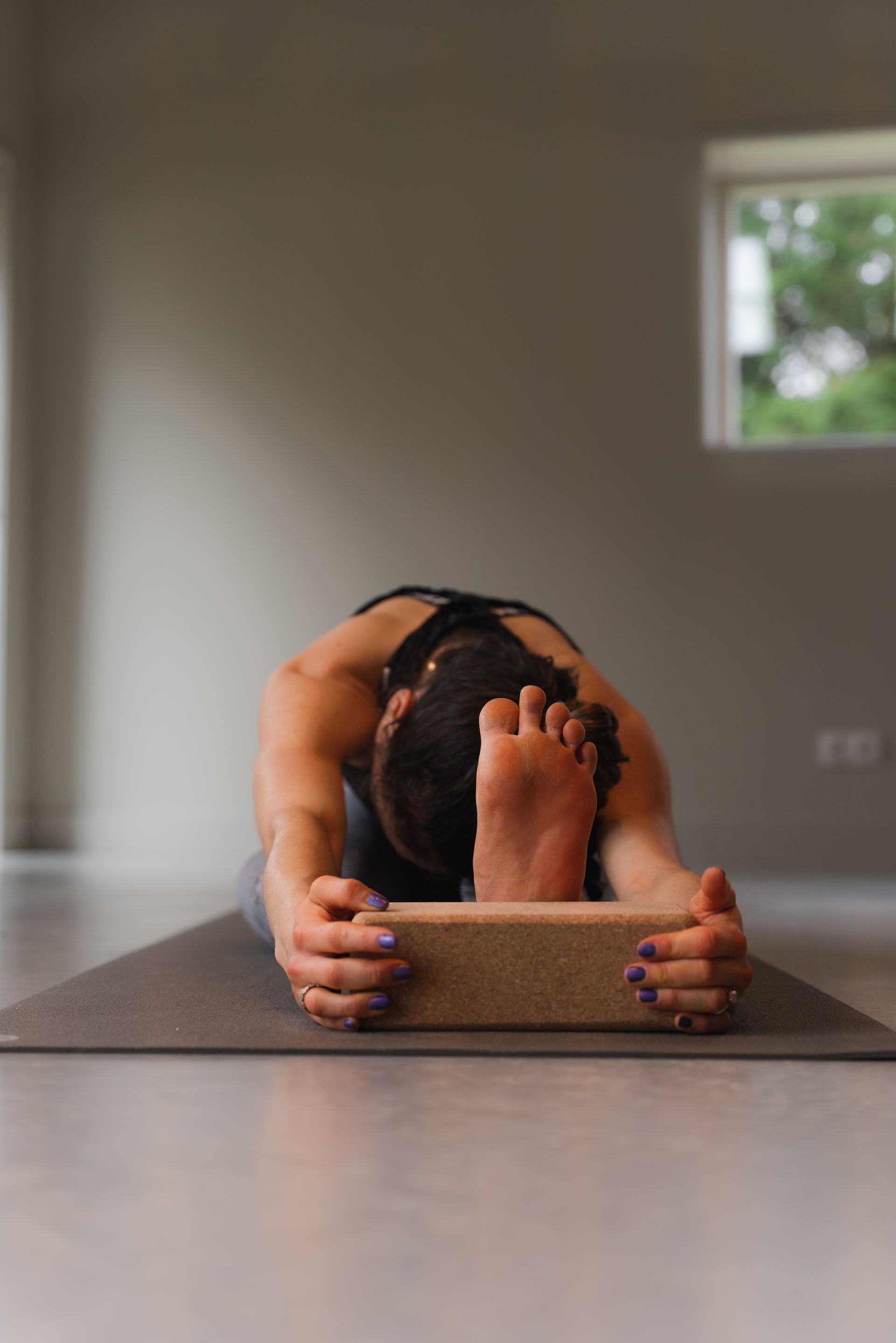 Person in yoga pose, hands on block, foot on head, gray mat.