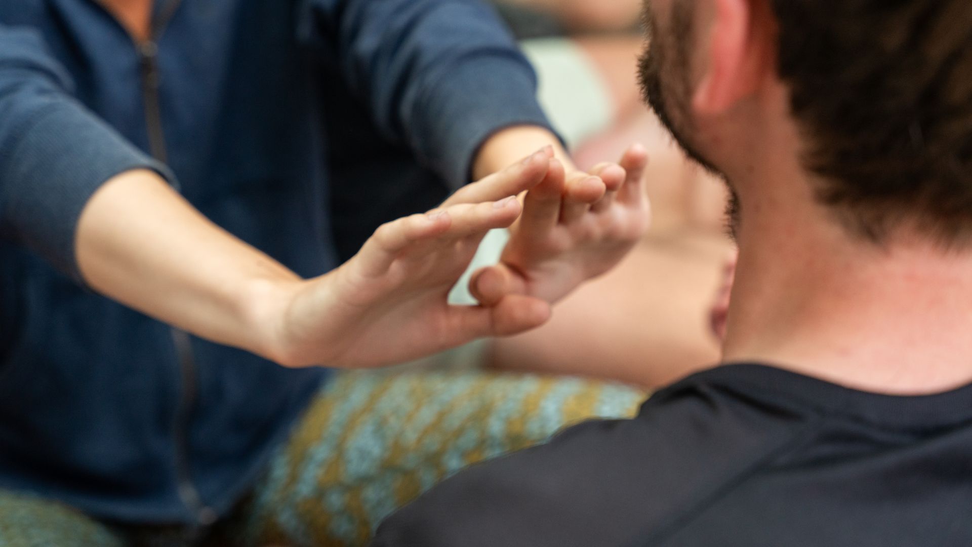Person's hands touching another's fingers. Both are indoors, person in focus has dark hair.