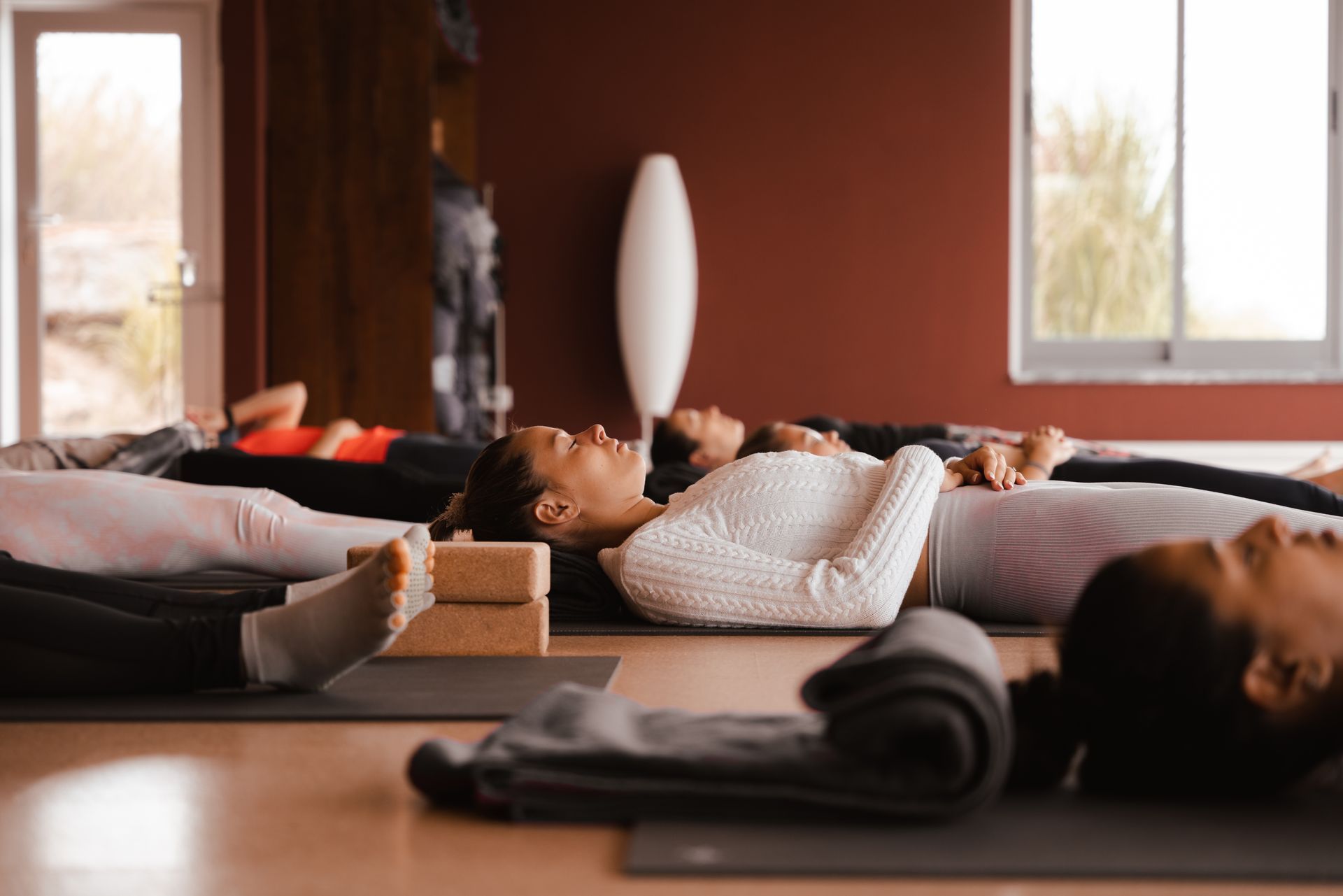 People lying on yoga mats with eyes closed in a studio.