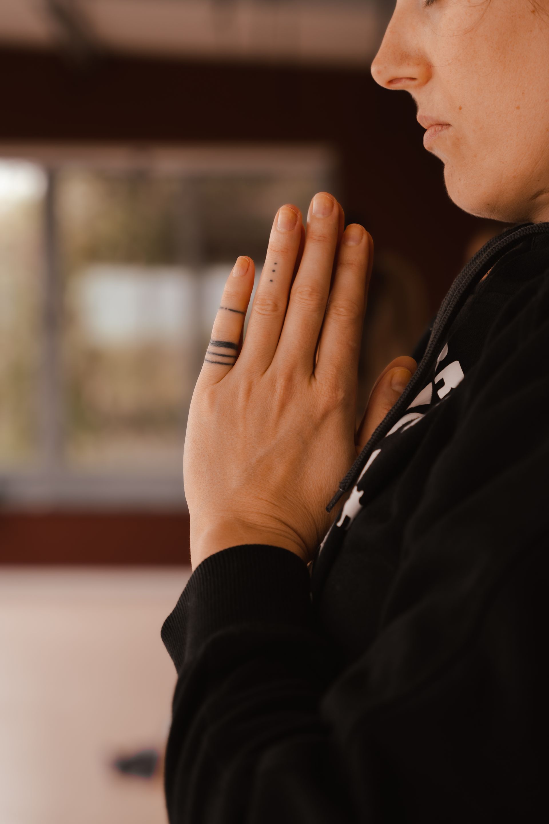 Person with hands together in prayer, a ring tattoo on a finger, indoors.