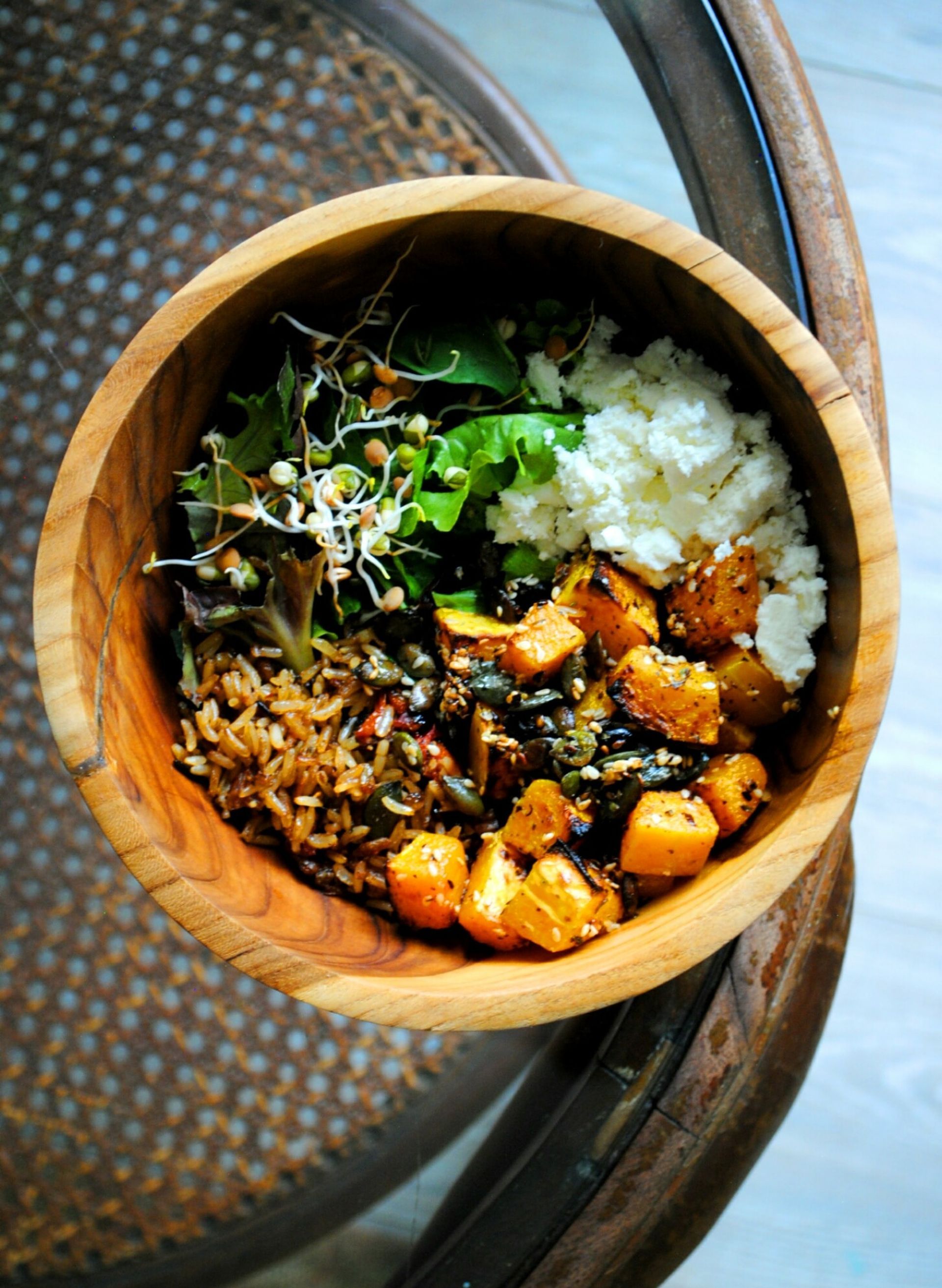 Wooden bowl filled with salad ingredients: roasted squash, greens, feta, lentils.