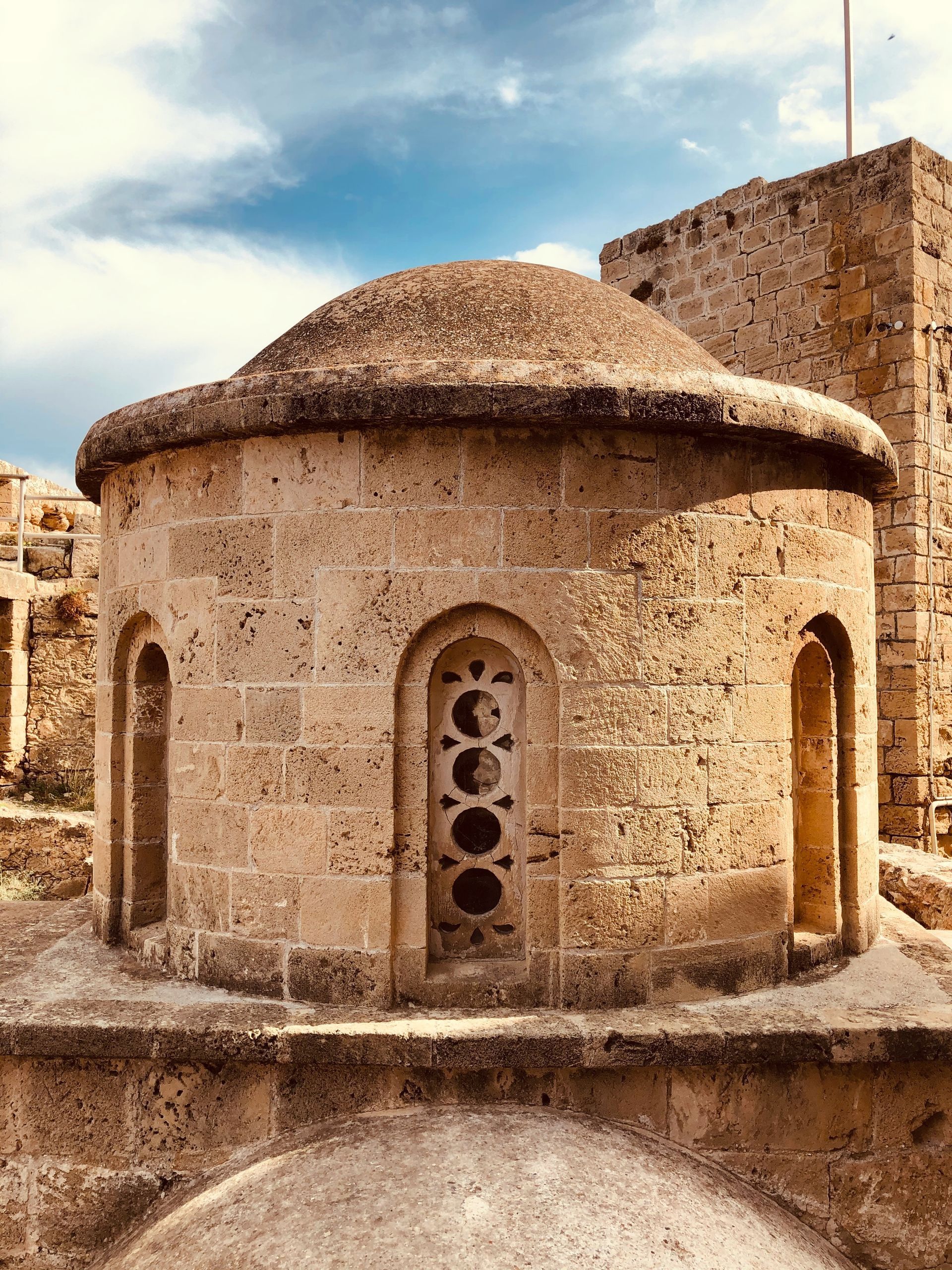 Stone-built domed structure with arched windows, possibly an ancient church or building, under a cloudy sky.