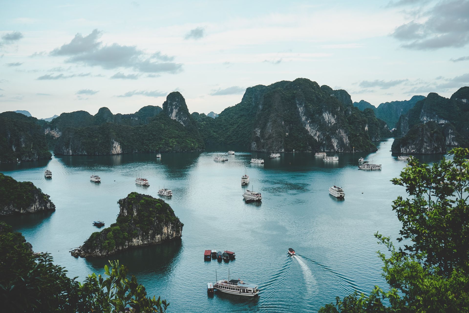 Bay with numerous limestone karsts and boats; overcast sky.