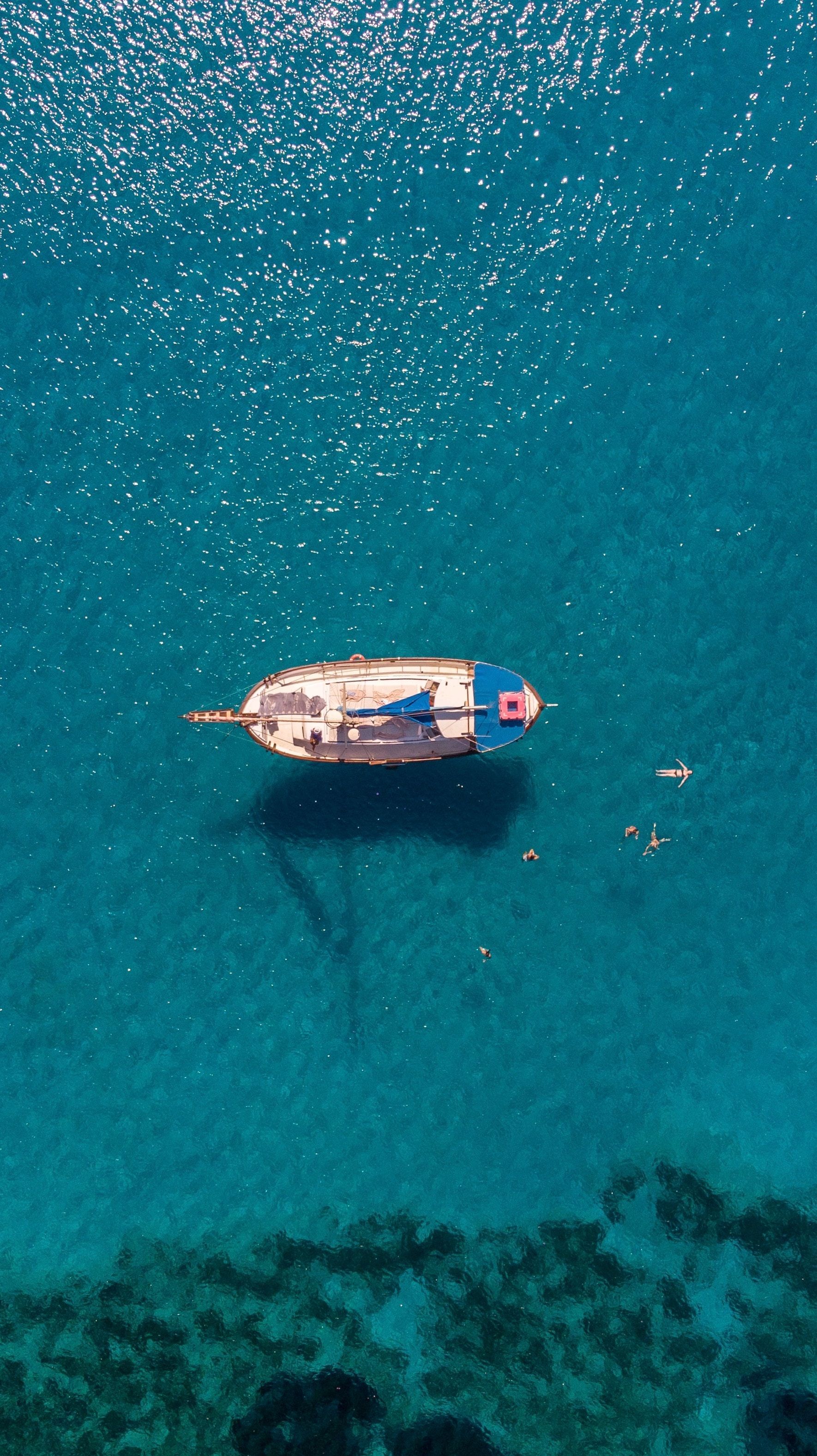 Boat floating in turquoise water with people swimming nearby. Sunny, overhead shot.