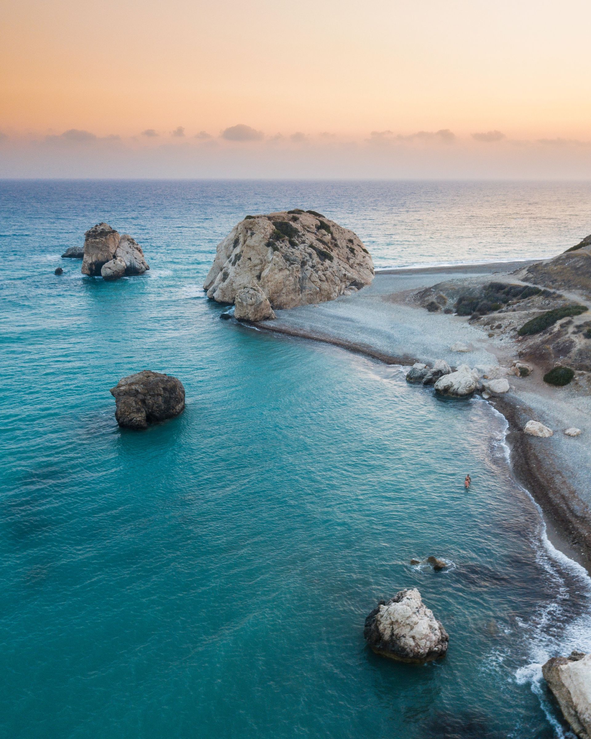 Turquoise sea with rock formations and beach under a sunset sky.