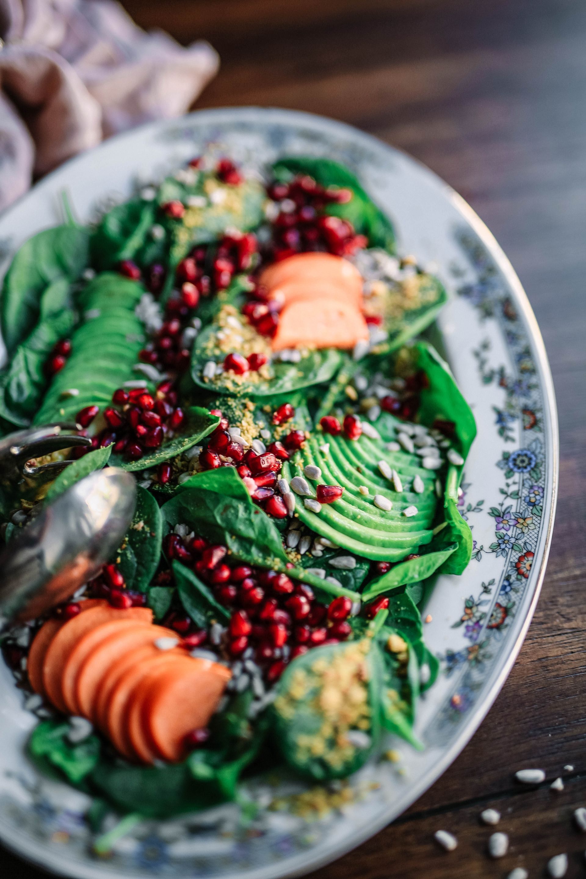 Salad on a decorative plate: spinach, avocado, pomegranate seeds, carrot slices.