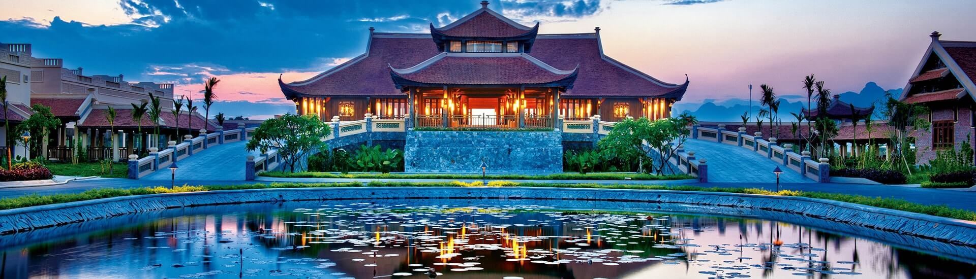 A tranquil Asian-style building reflecting in a pond at dusk.