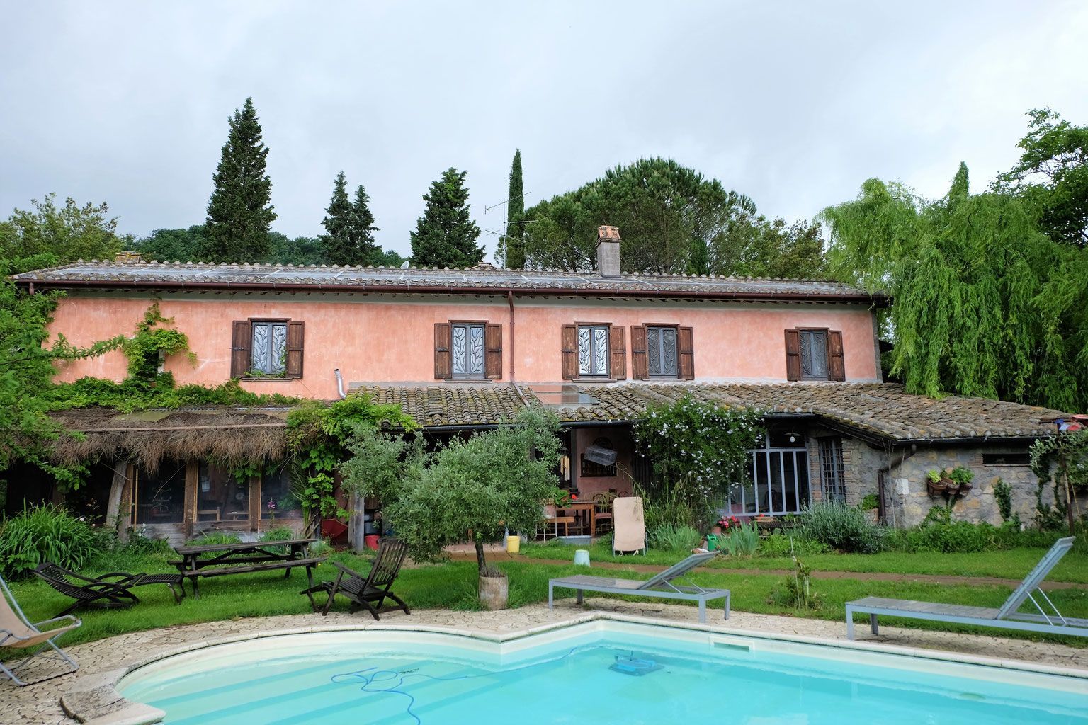 A two-story pink stucco house with brown shutters and a pool in a green yard.