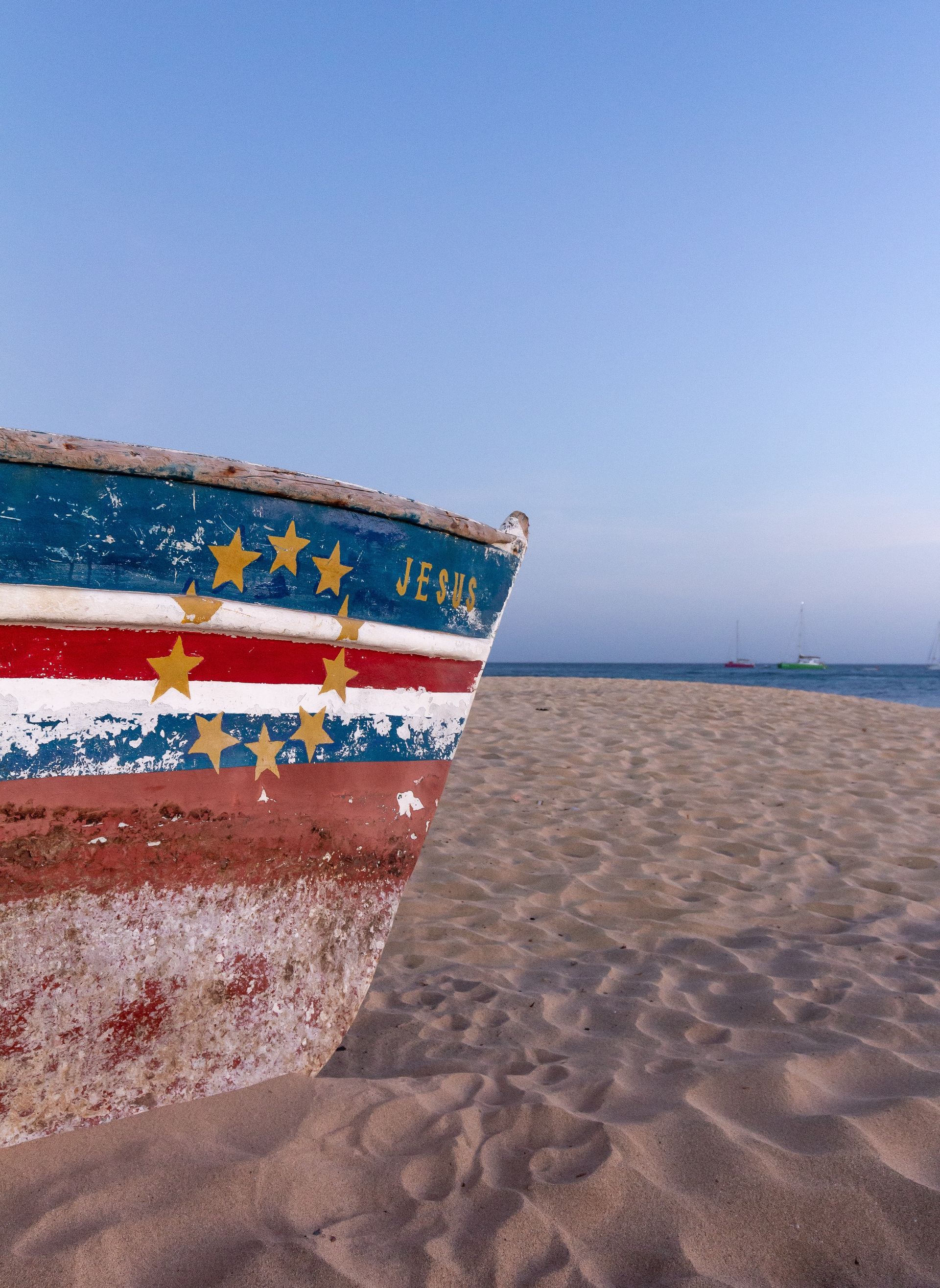 Boat painted with Cape Verde flag on sandy beach under blue sky.