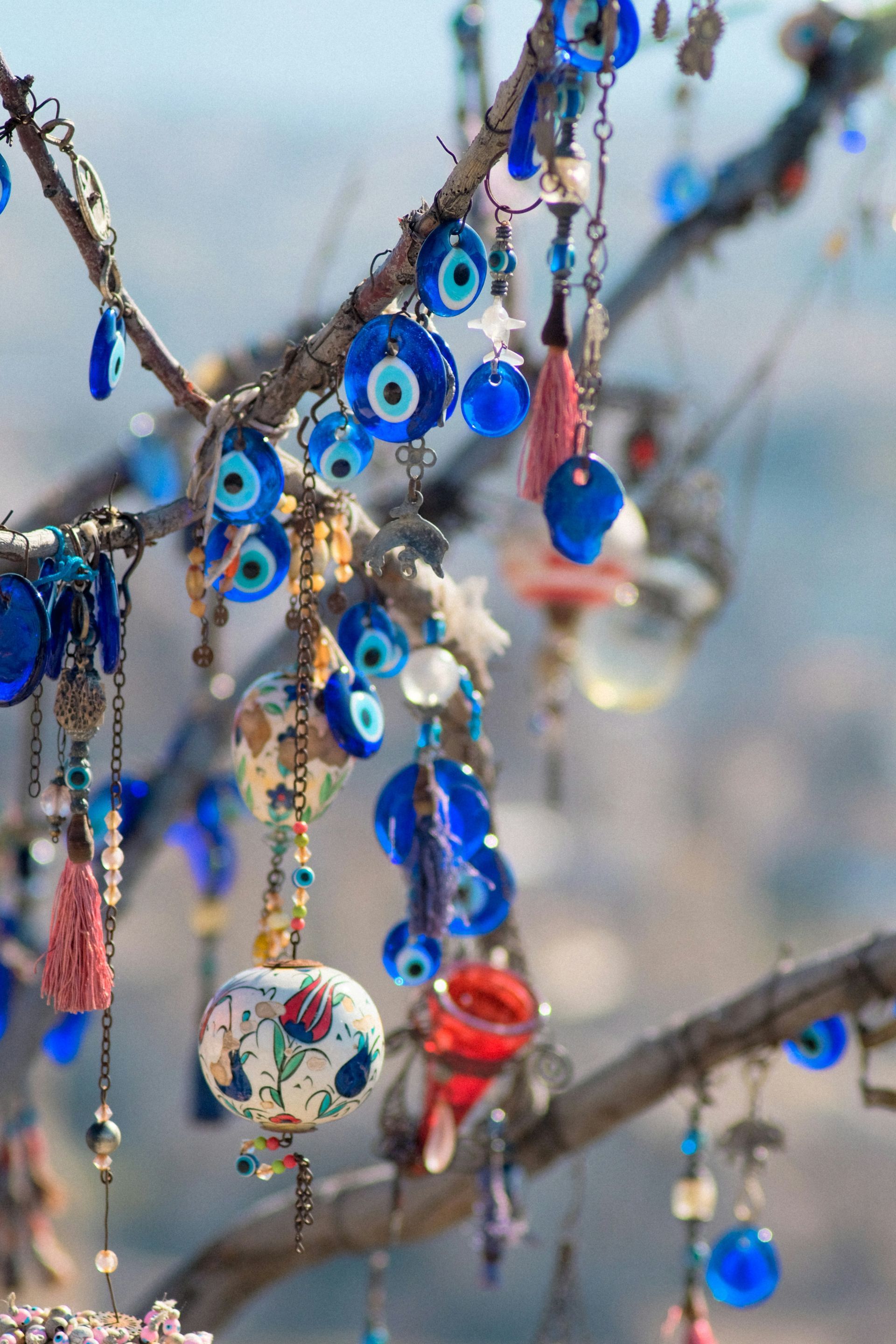 Branches adorned with blue evil eye charms, tassels, and decorative glass orbs against a blurred background.