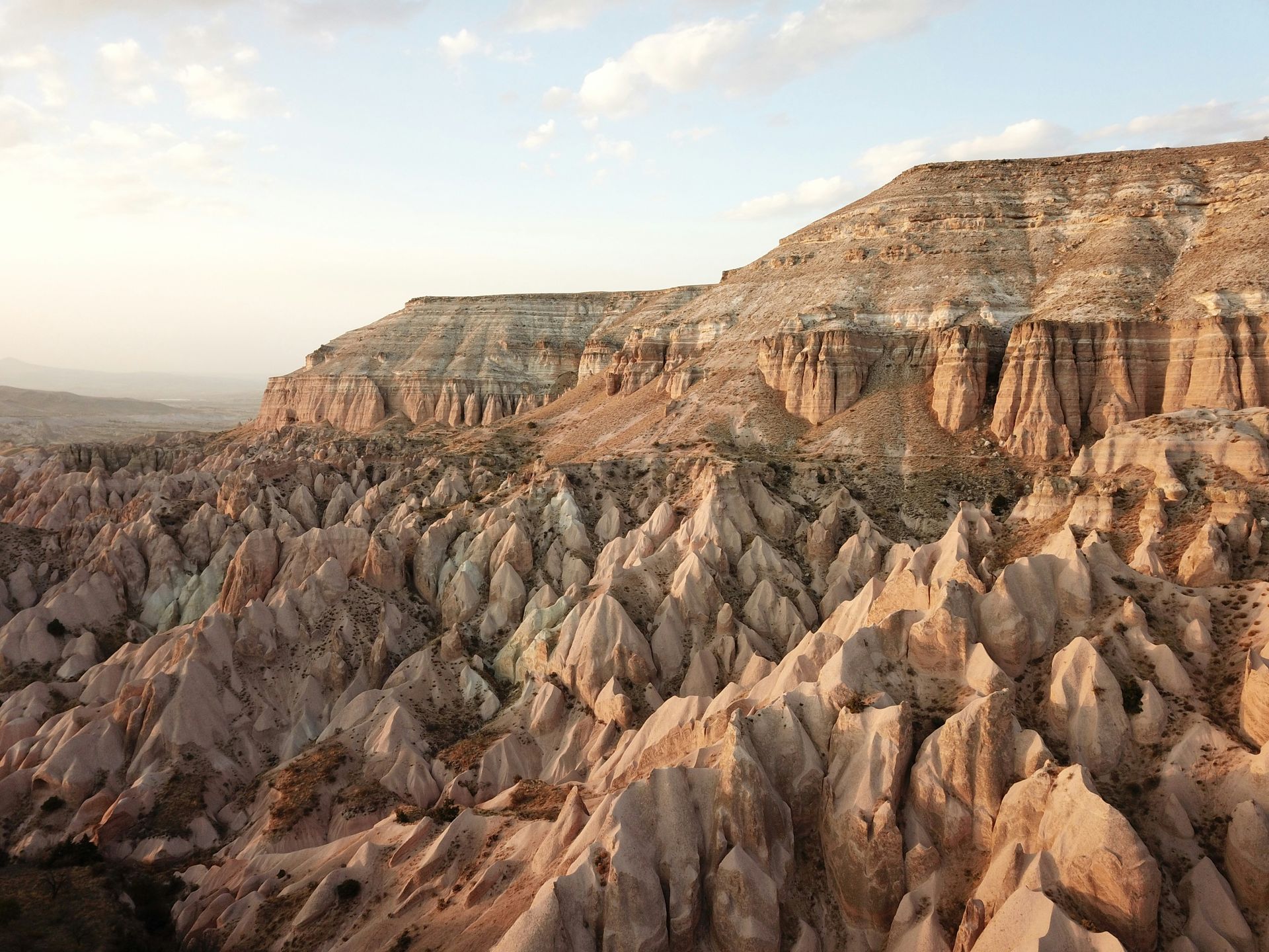 Rocky, eroded landscape of Cappadocia, Turkey. Light brown and beige rock formations under a cloudy sky.