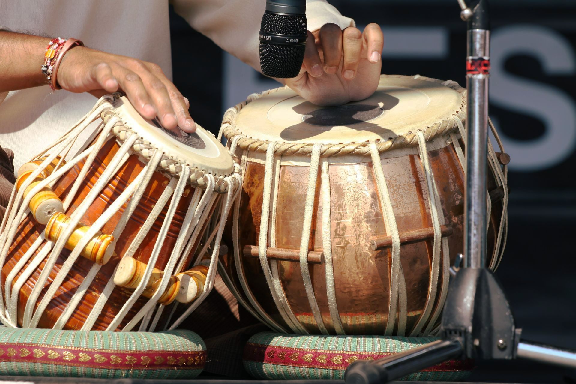 Close-up of tabla drums being played. Brown wooden drums, hands visible, microphone.