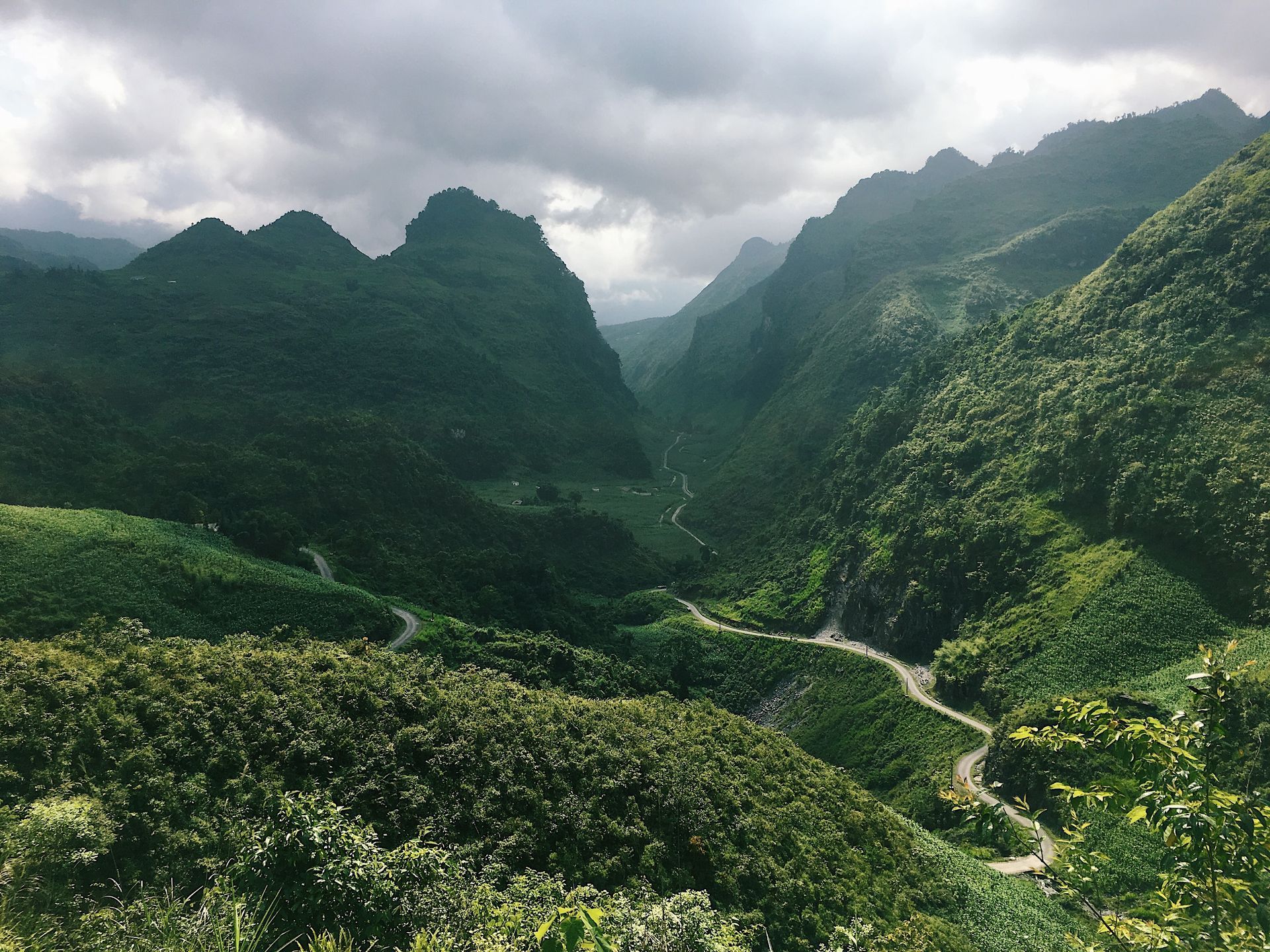 Green mountain valley with winding road, under cloudy sky.