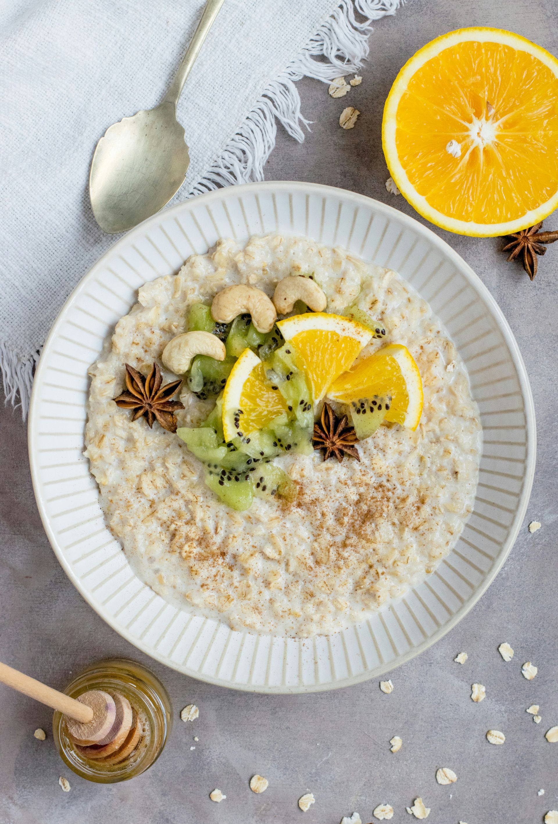 Oatmeal topped with orange slices, kiwi, cashews, and star anise, drizzled with honey.
