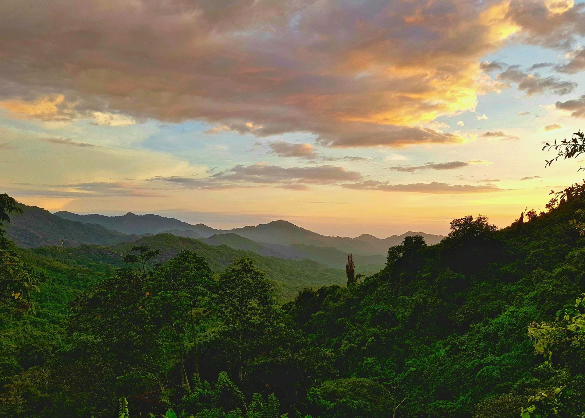 Sunset over lush green mountain range with colorful sky.