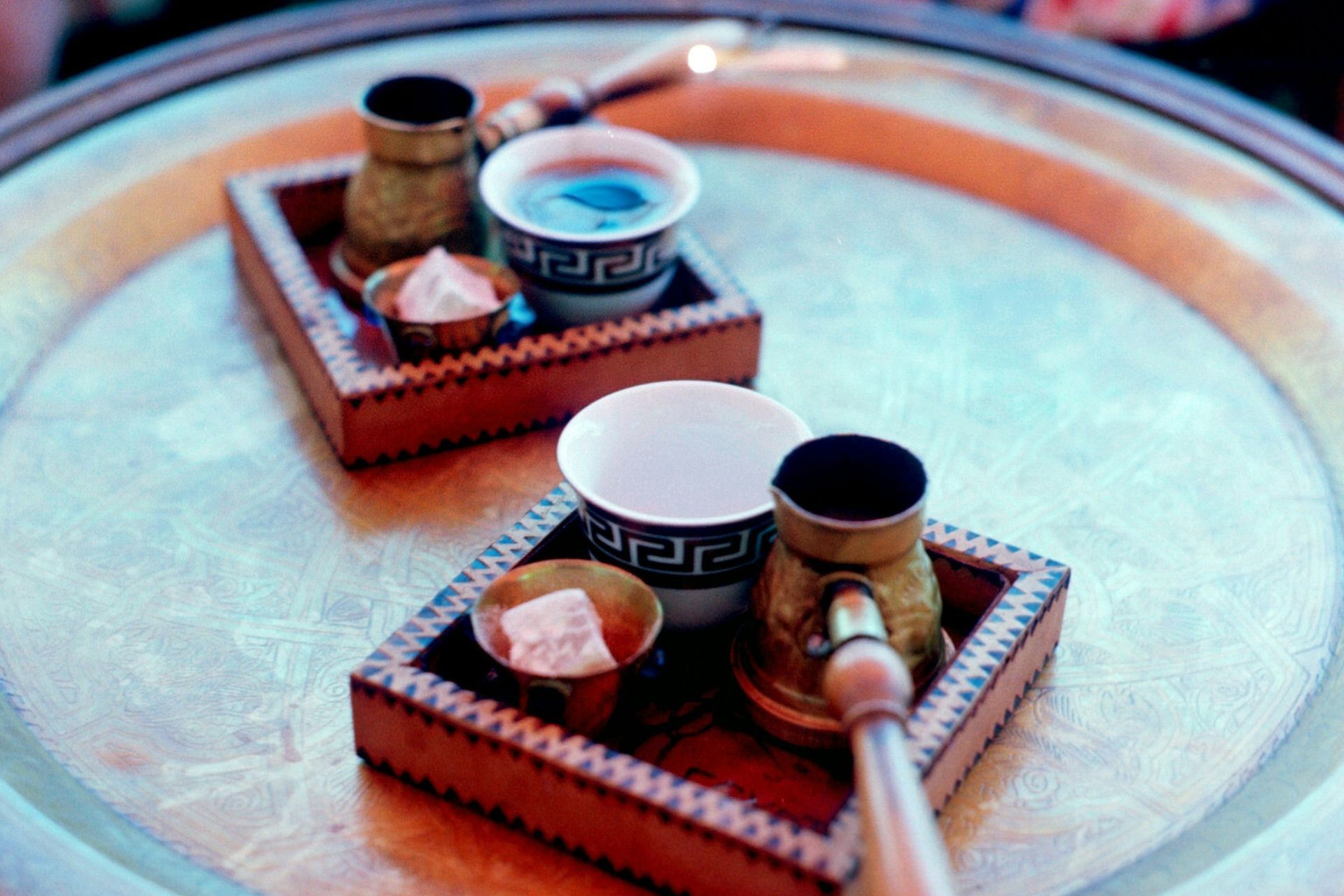 Two trays with coffee cups, small pots, and sweets on a silver platter.