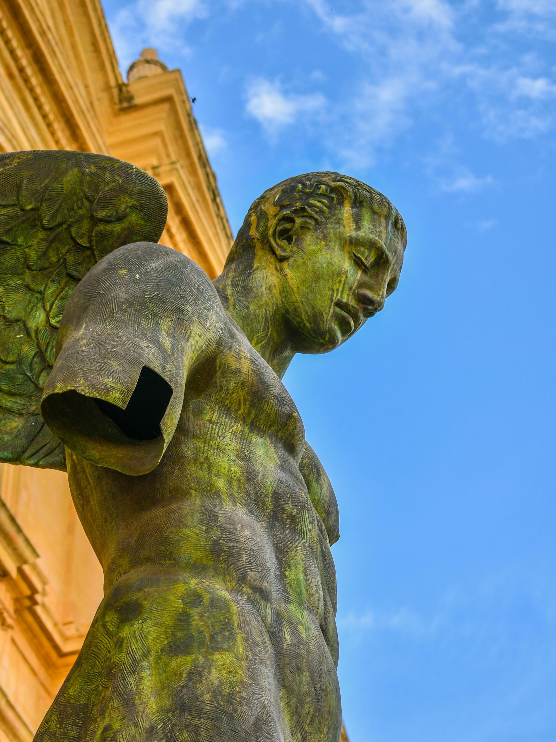 Stone angel statue with mossy green wings and weathered torso, set against a blue sky.