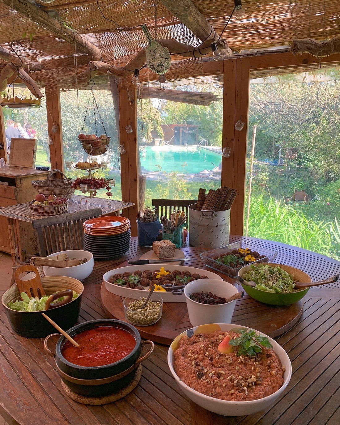 Table of food with outdoor setting. Various dishes, including salad, dips, and sides. Sunlight streams through.