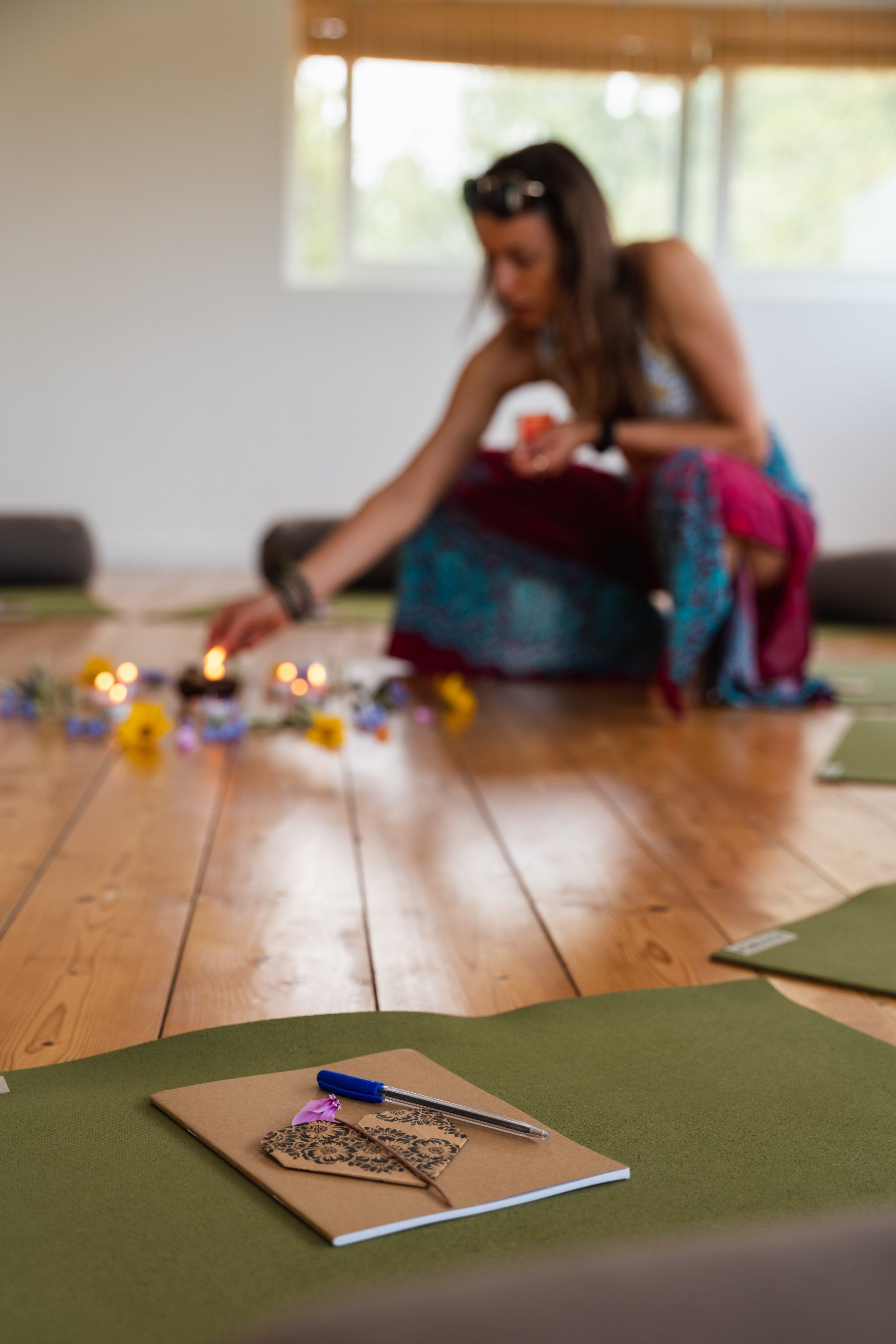 Woman placing candle near flowers and journals on yoga mats in a bright studio.