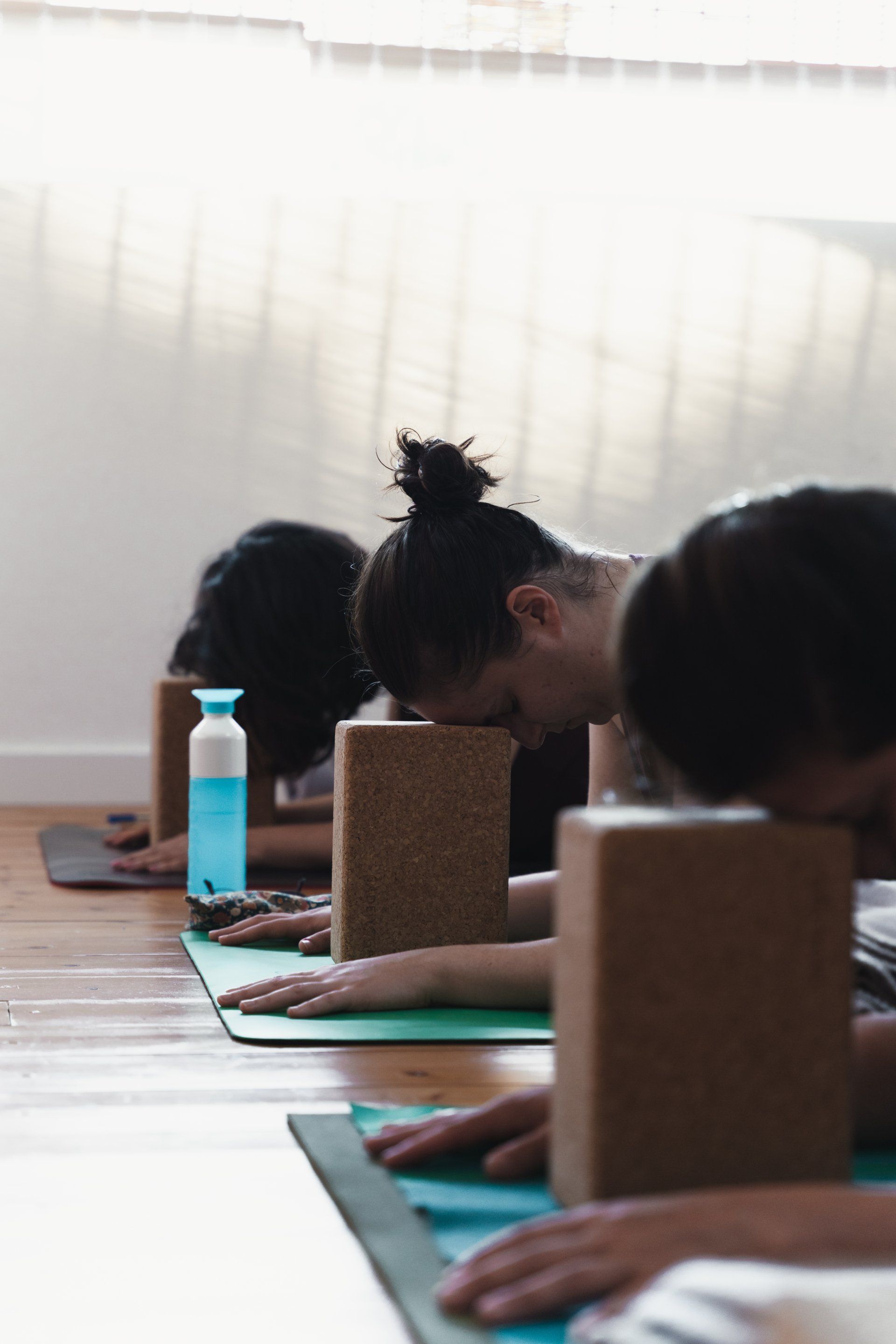 People in yoga class, leaning forward on blocks, near a window.