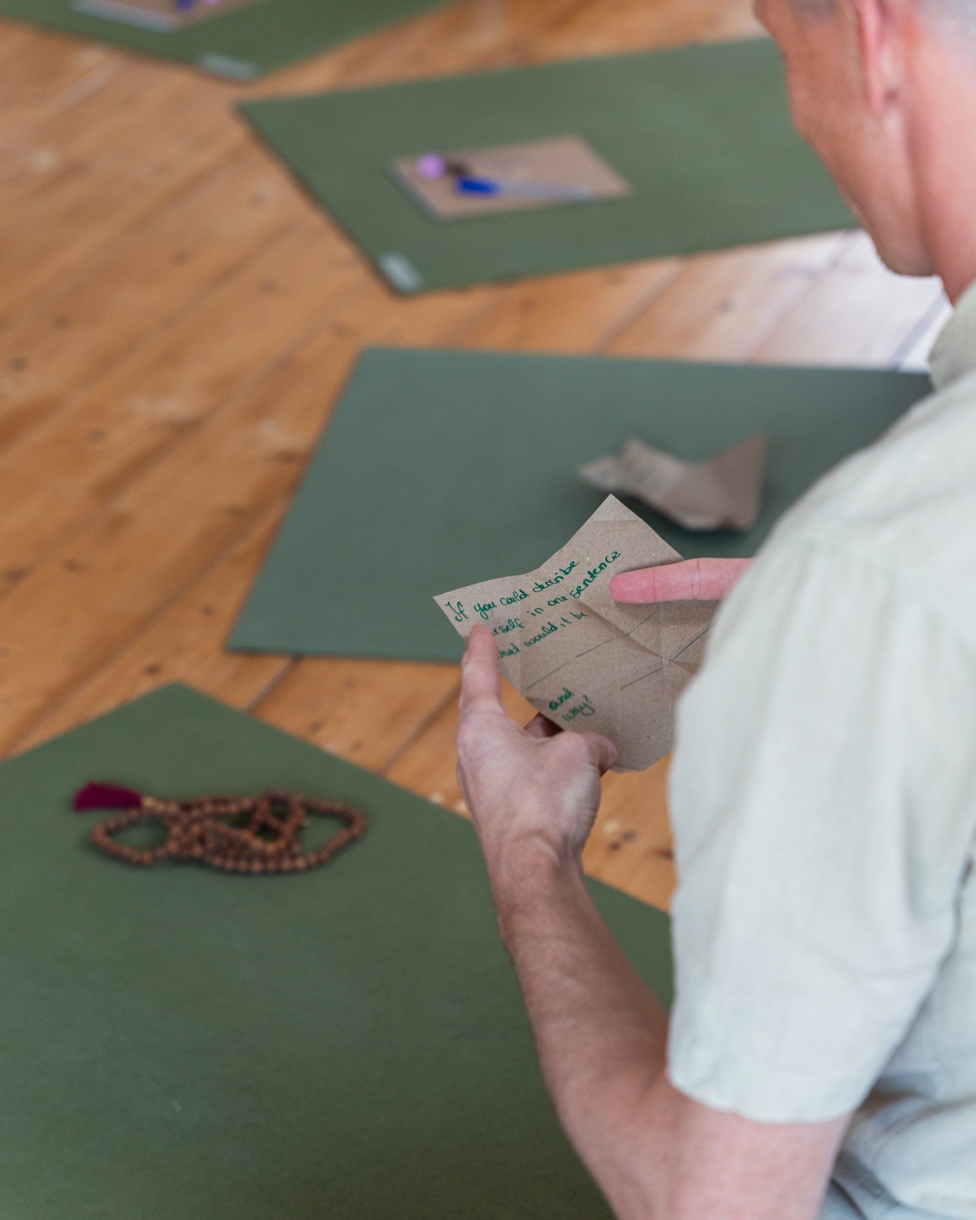 Man holding paper, pointing; yoga mats on wooden floor in background.